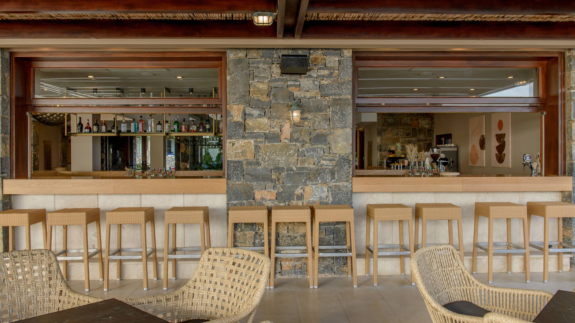 Stylish outdoor resort bar with wicker seating, stone wall, and bamboo ceiling.
