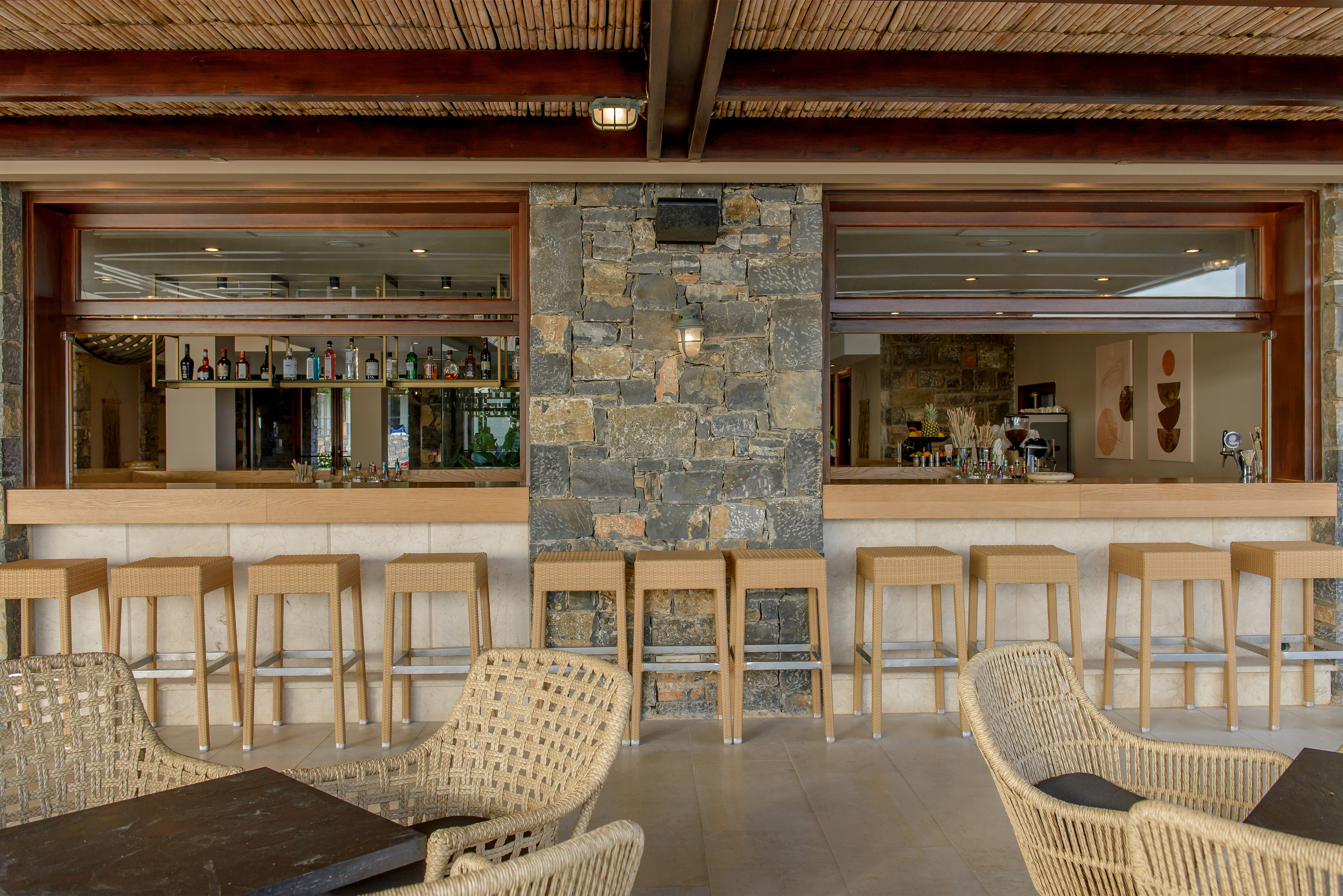 Stylish outdoor resort bar with wicker seating, stone wall, and bamboo ceiling.