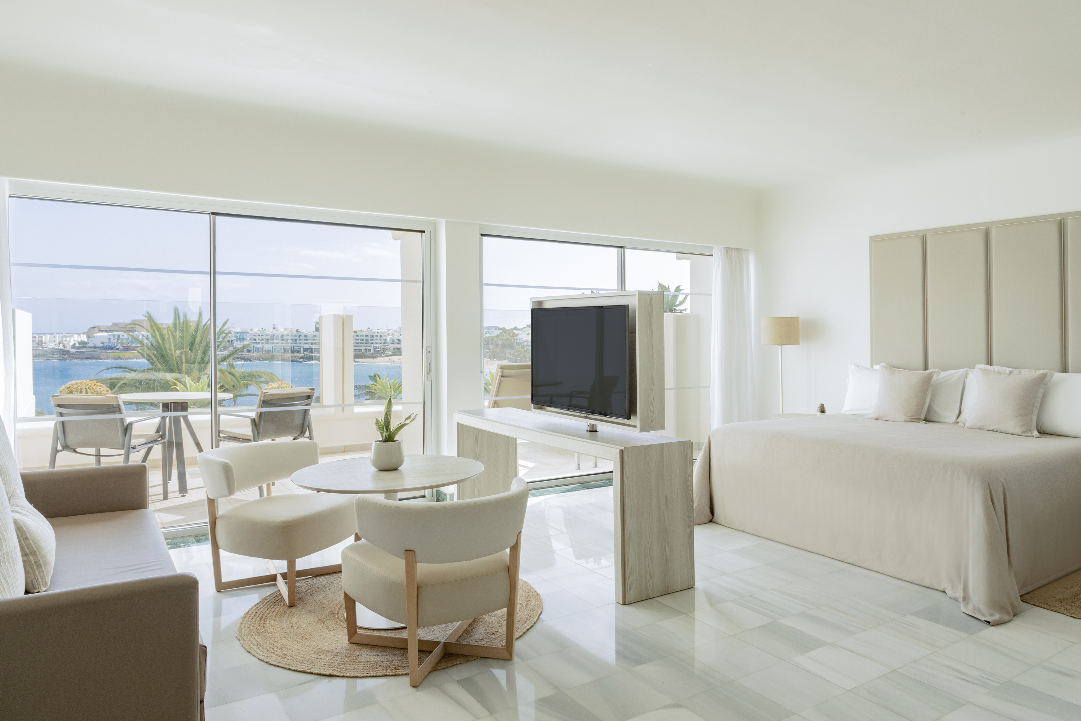 Spacious modern hotel suite with ocean view, balcony, bedroom, and living area.