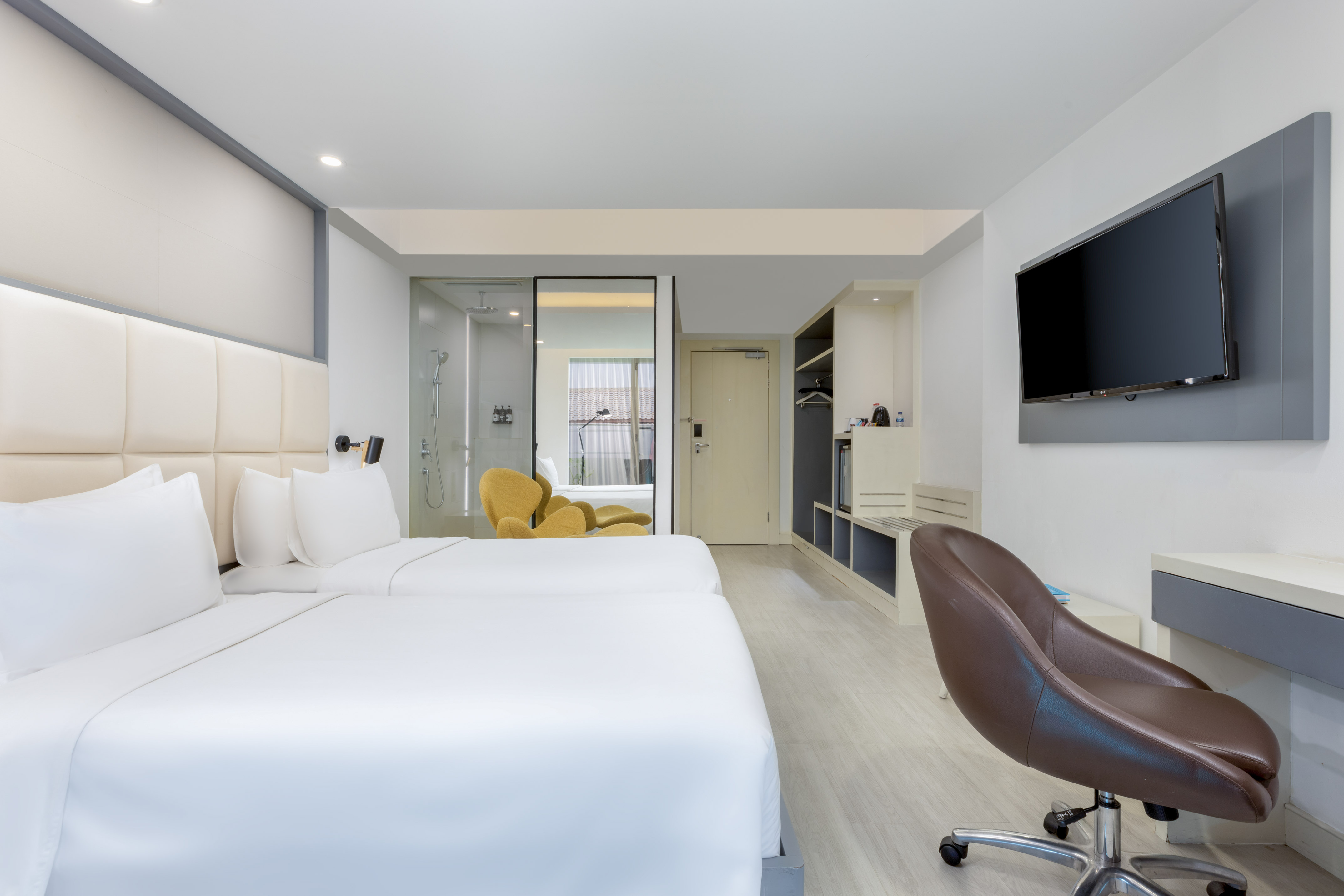 Bright modern hotel room with two twin beds, glass shower, desk, and TV.