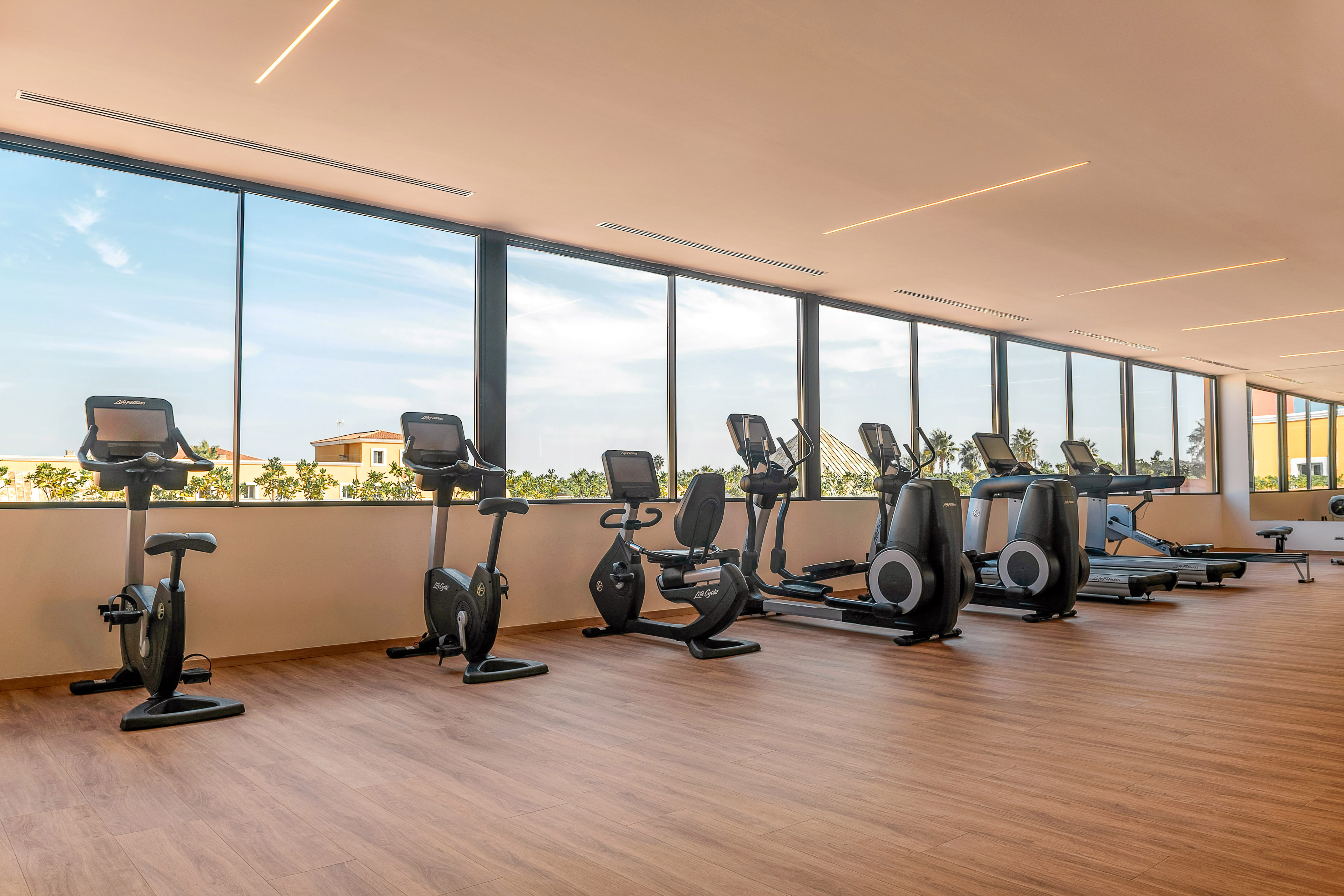 Modern gym with exercise bikes, ellipticals, treadmills, and large scenic windows.