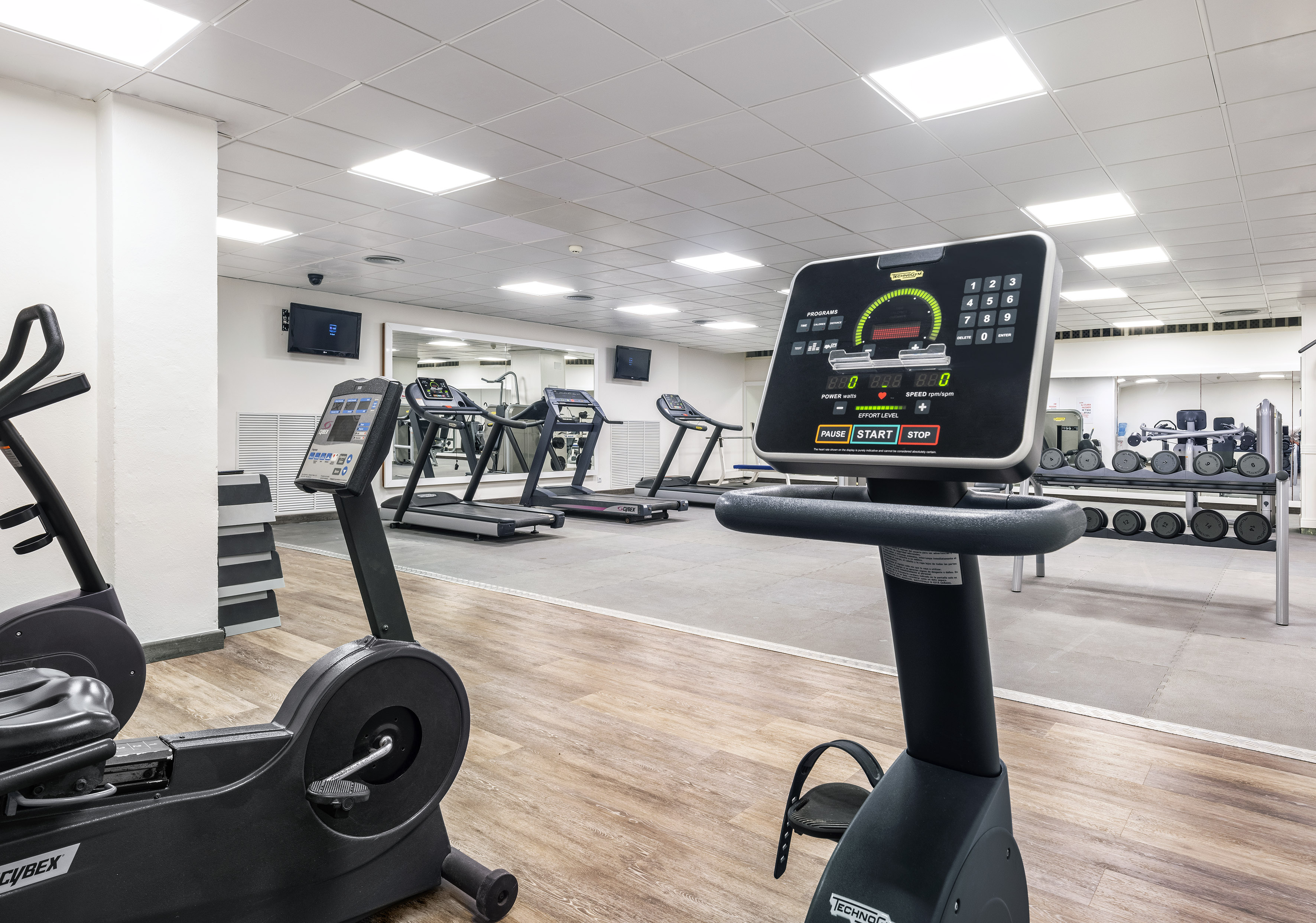 Well-lit gym with Technogym bikes, treadmills, and dumbbells.