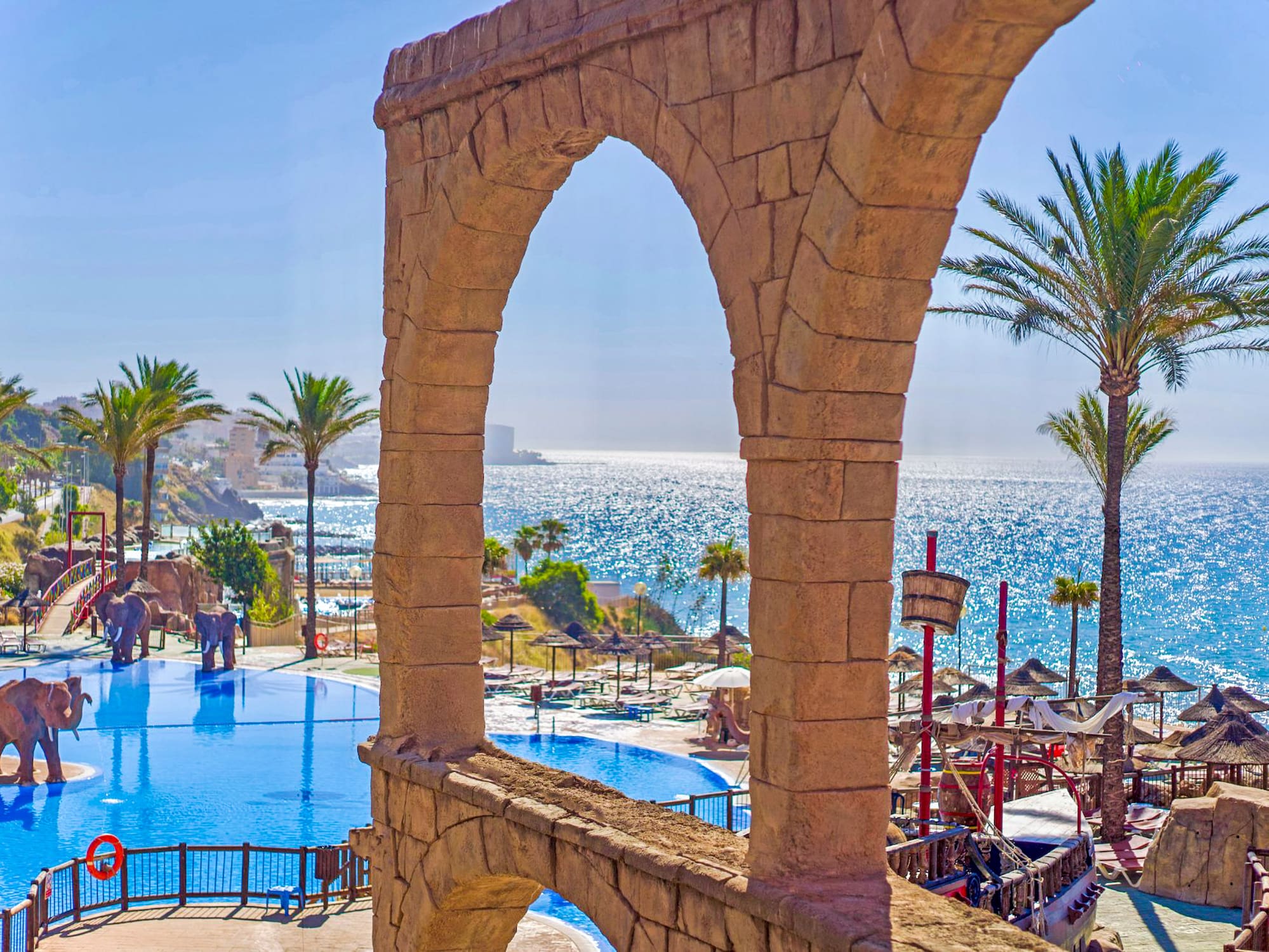 a pool with a stone arch and palm trees