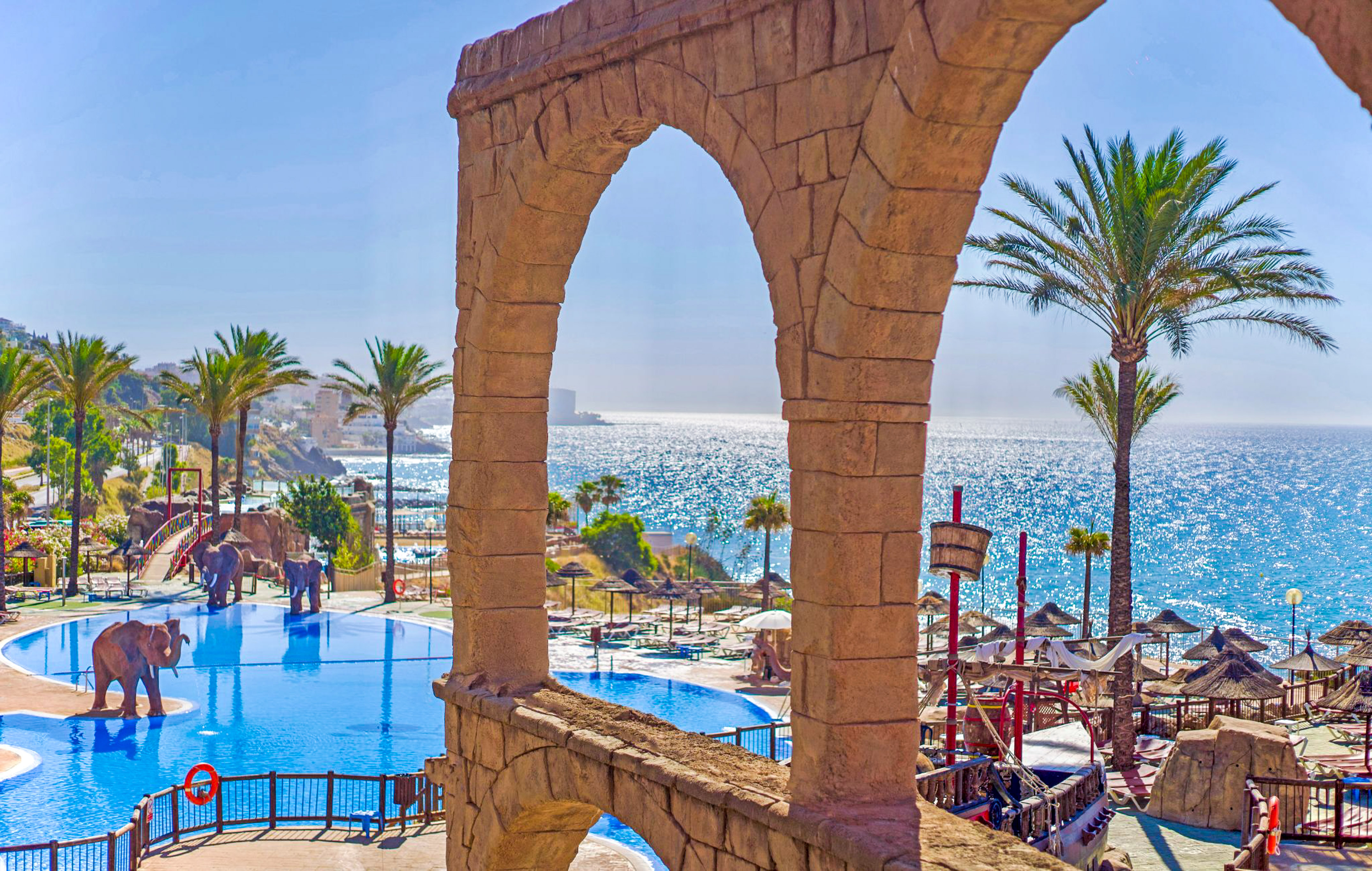 a pool with a stone arch and palm trees