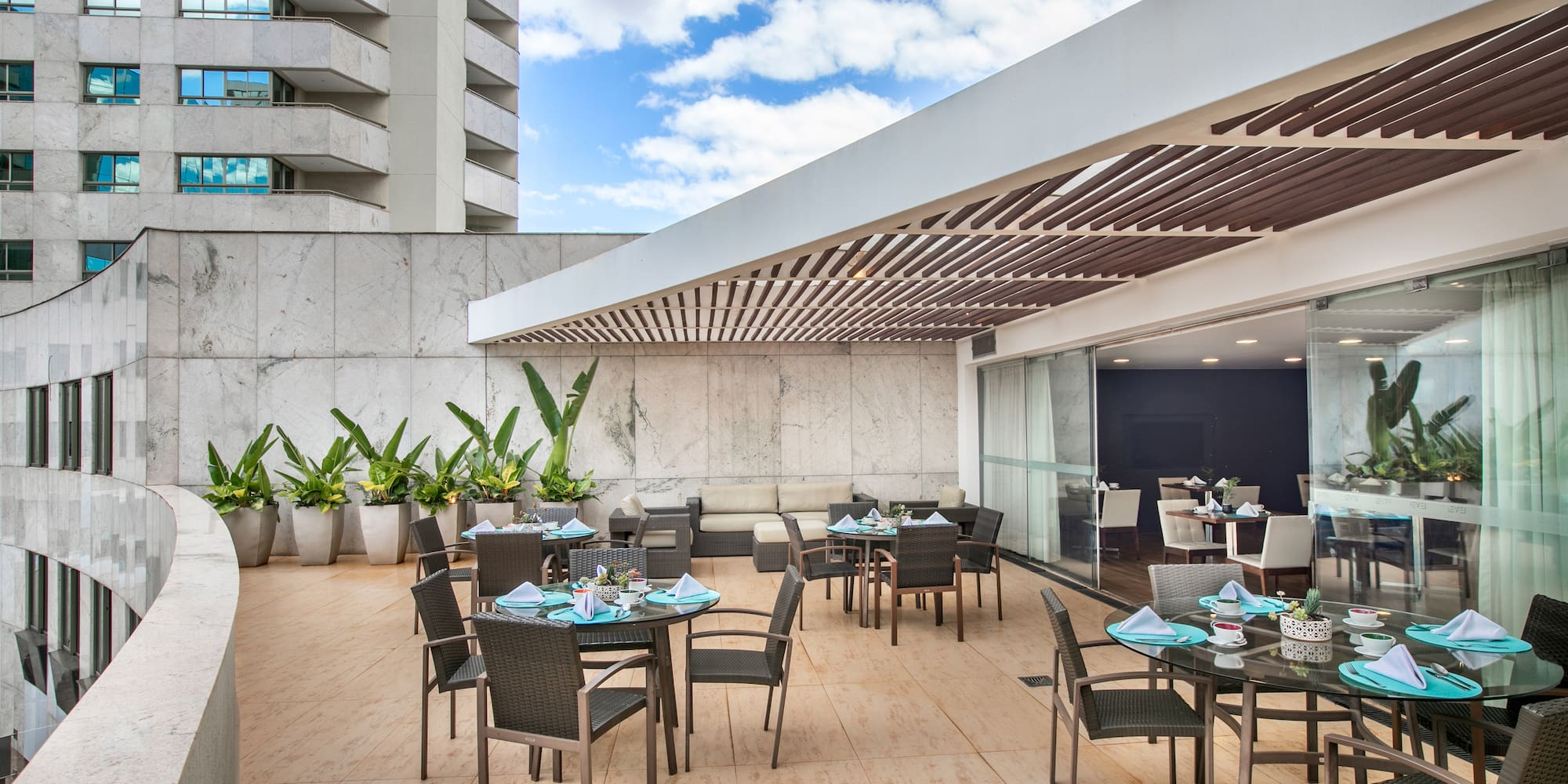Modern outdoor dining terrace with tables, chairs, plants, and city architecture.