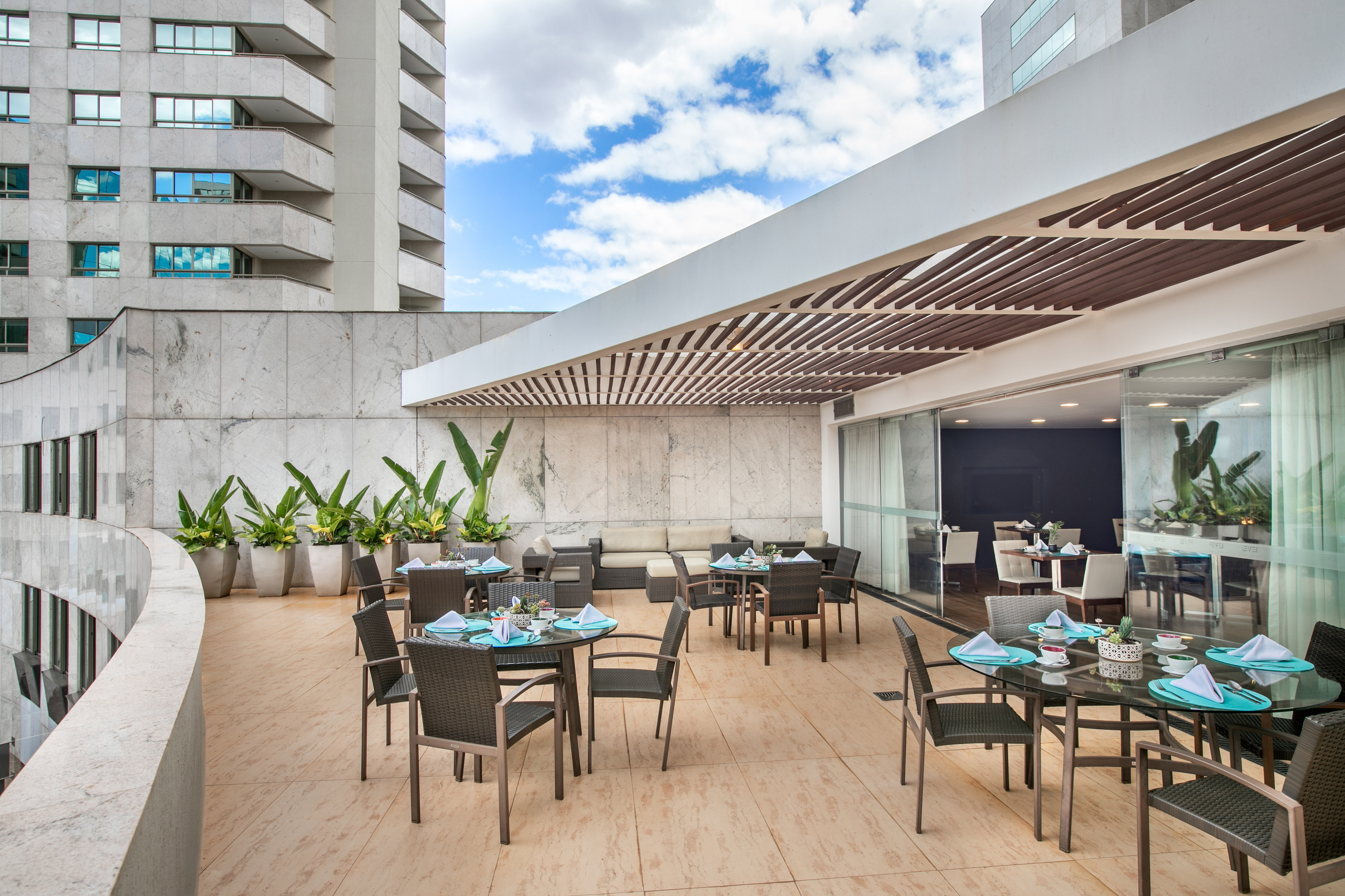 Modern outdoor dining terrace with tables, chairs, plants, and city architecture.