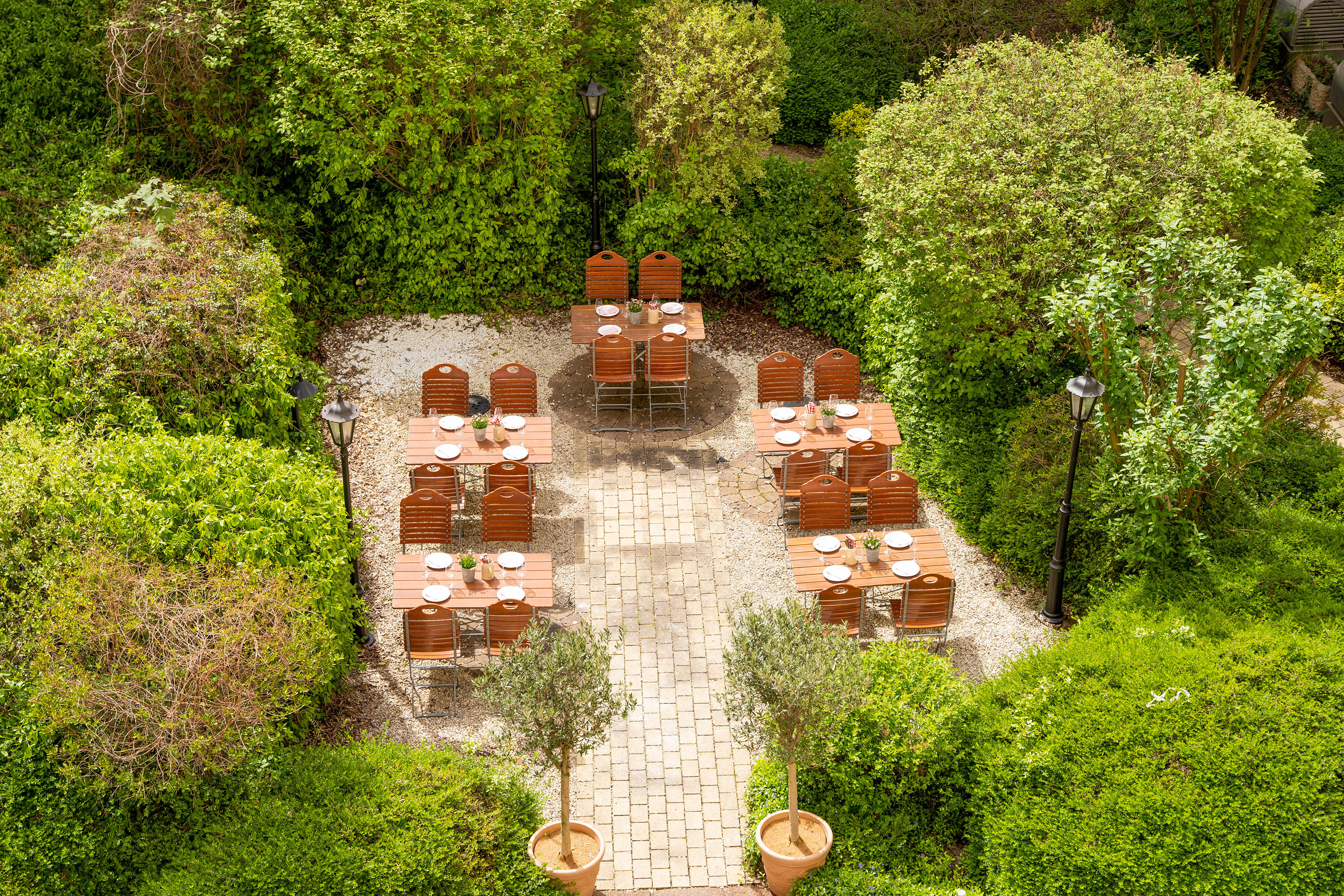 Lush garden courtyard with outdoor dining tables, chairs, and paved walkway.