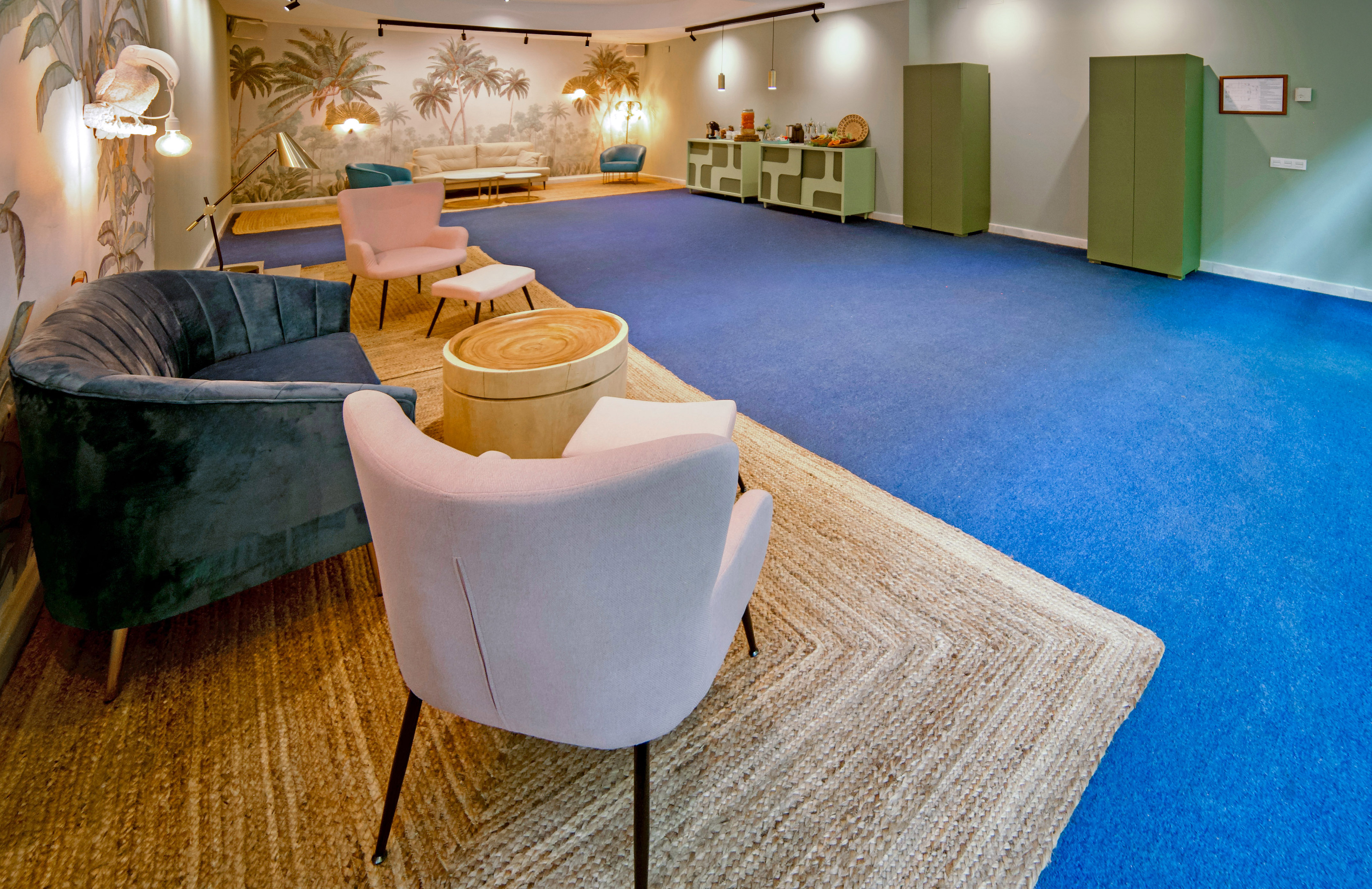 Spacious modern lounge with blue carpet, palm wallpaper, and colorful armchairs.