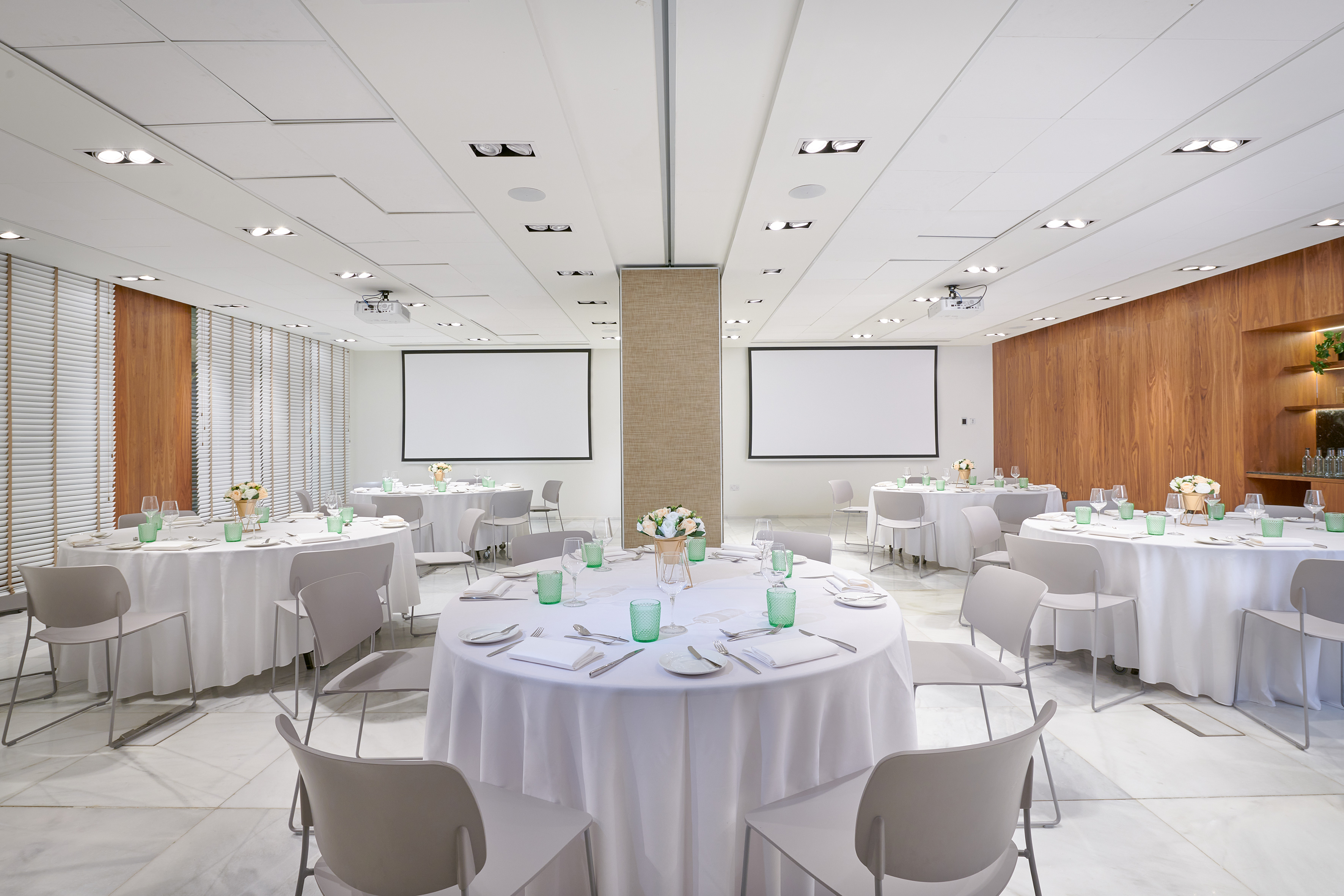 Modern conference room with round tables, white chairs, and two projection screens.