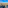 Aerial city view: residential buildings, streets, distant skyline, bright blue sky.