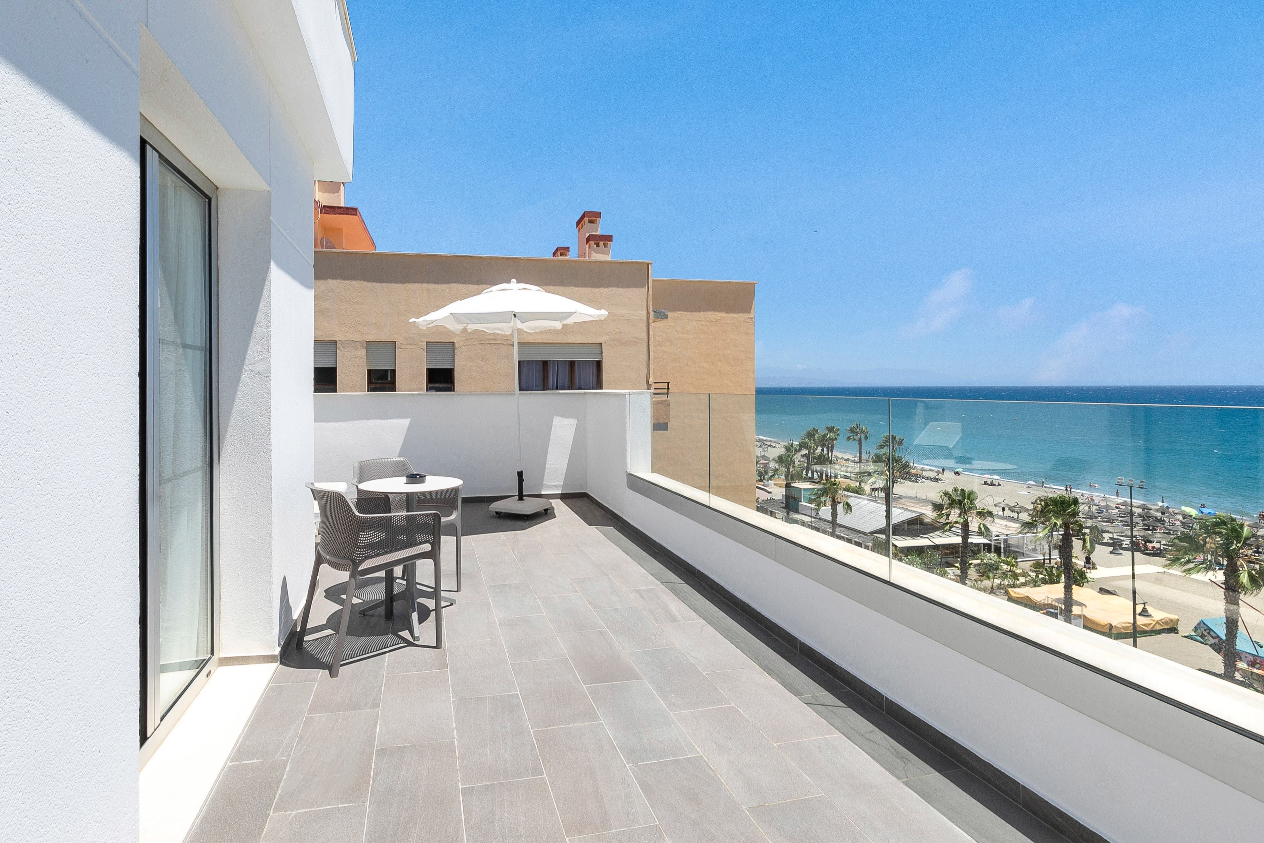 Modern balcony with outdoor seating overlooking beach and blue sea.