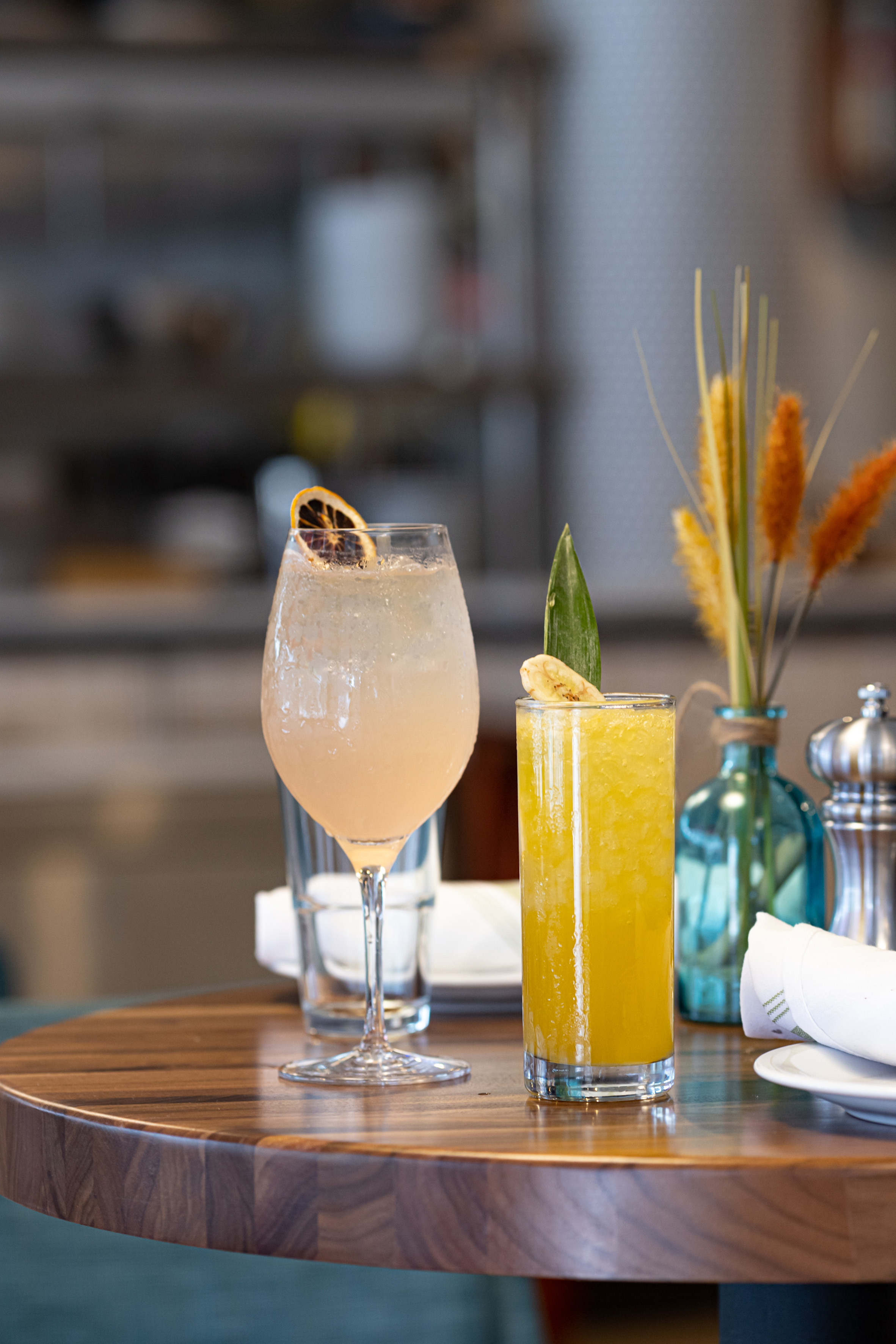 Two cocktails with orange and banana garnishes on a wooden table.