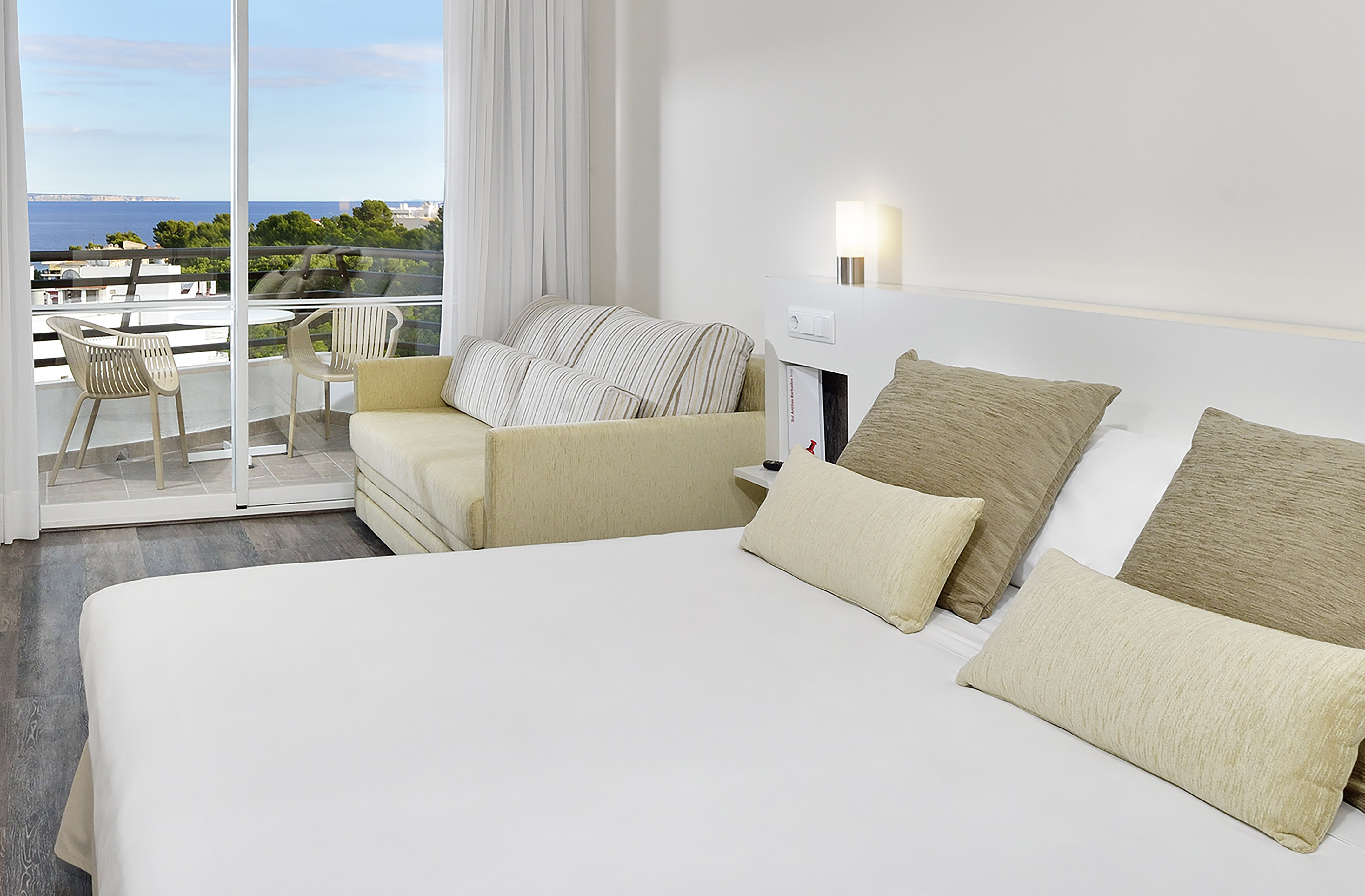 Modern hotel room with balcony, sea view, sofa, and large bed.