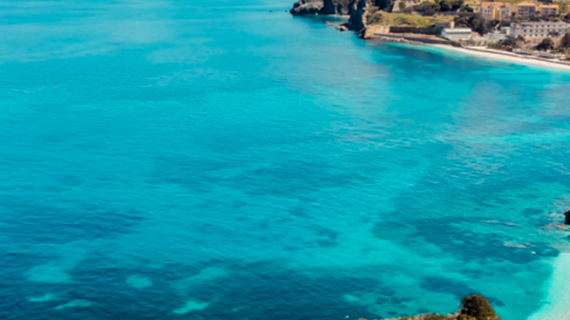 Turquoise sea with coastal town, ancient fortress, mountains, and rocky island.
