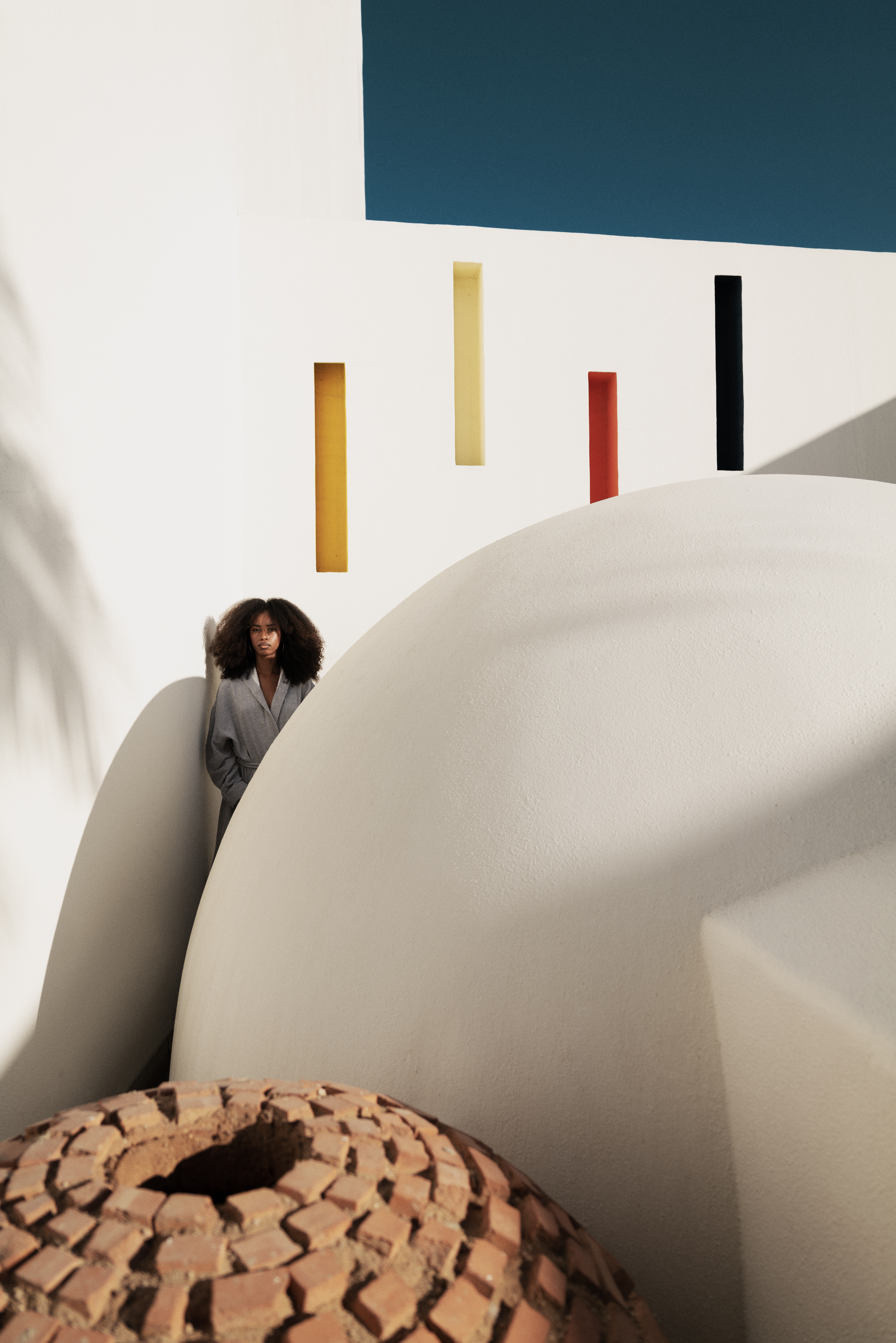 Woman with curly hair against white modern architecture and colorful wall accents.