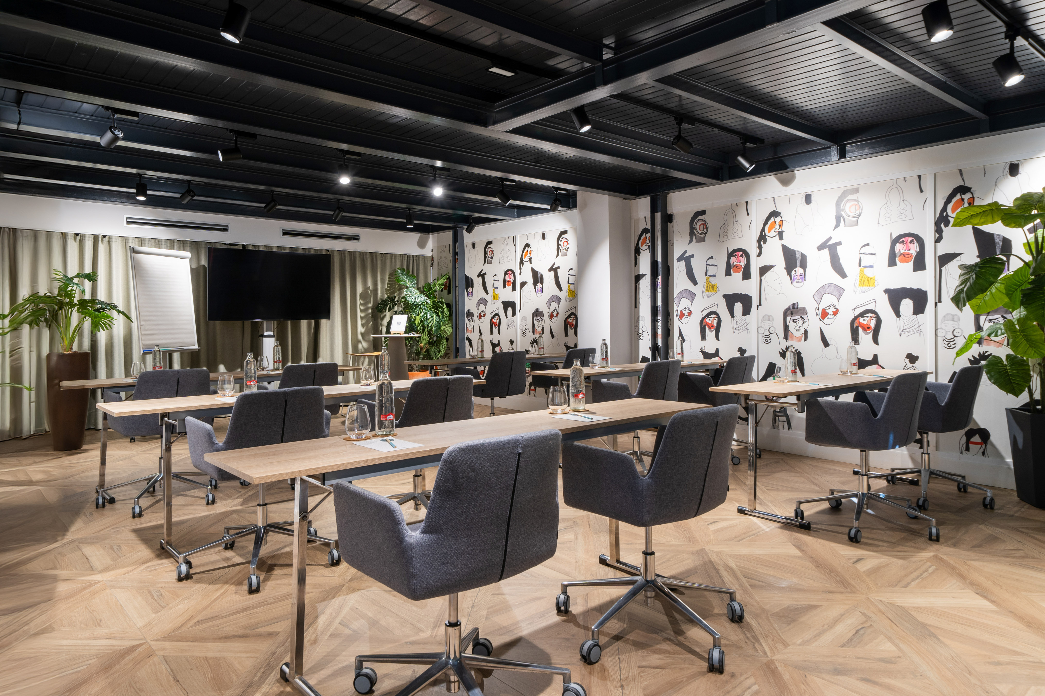 Modern meeting room with abstract art walls, gray chairs, wood floor, TV.