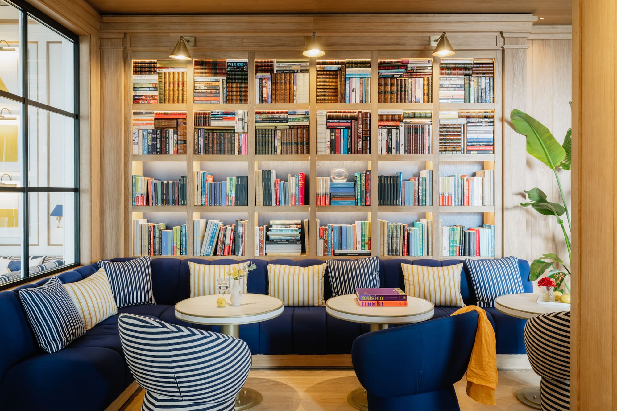 Stylish library lounge: wooden bookshelf, blue sofa, striped seating.