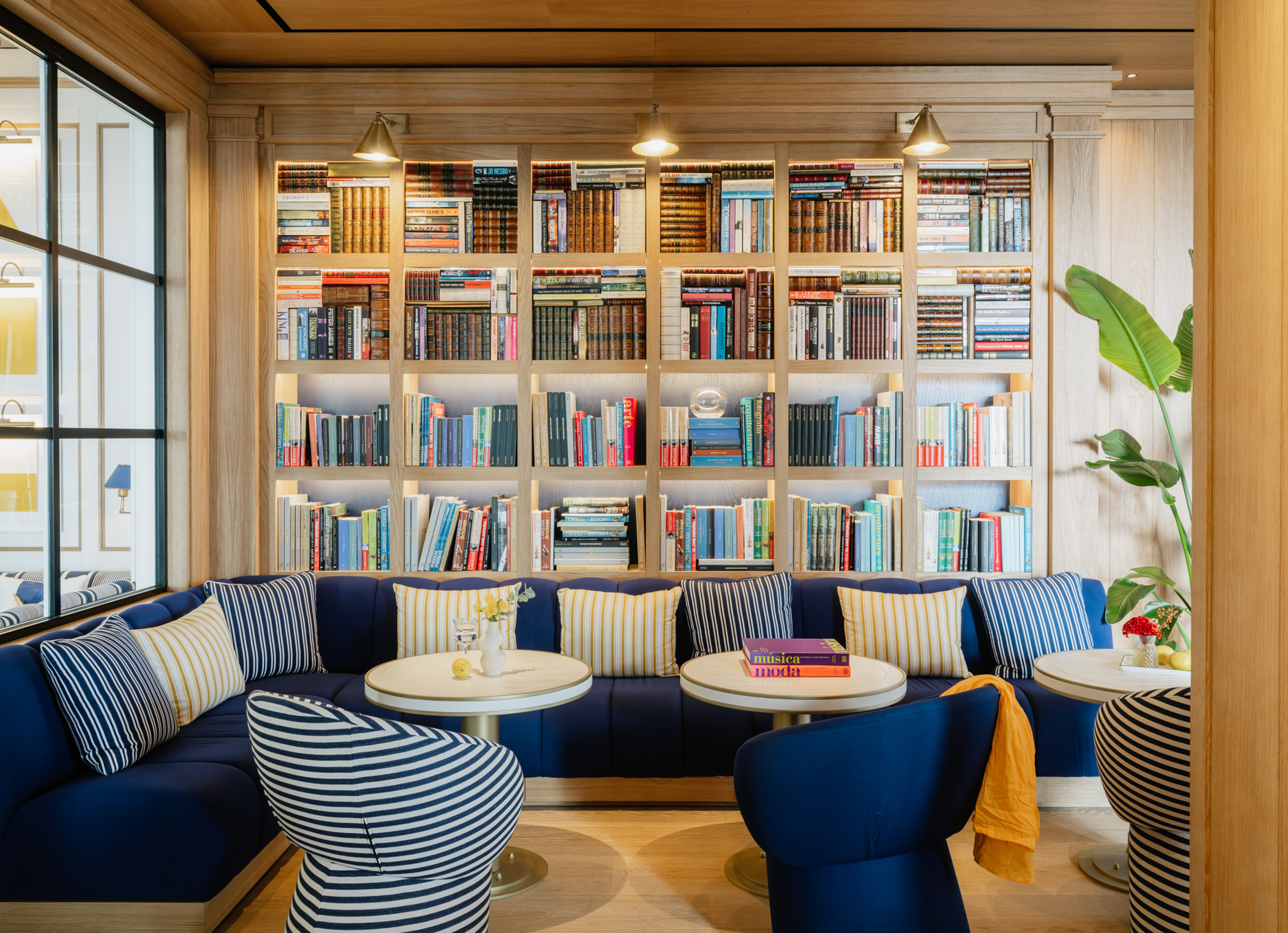 Stylish library lounge: wooden bookshelf, blue sofa, striped seating.