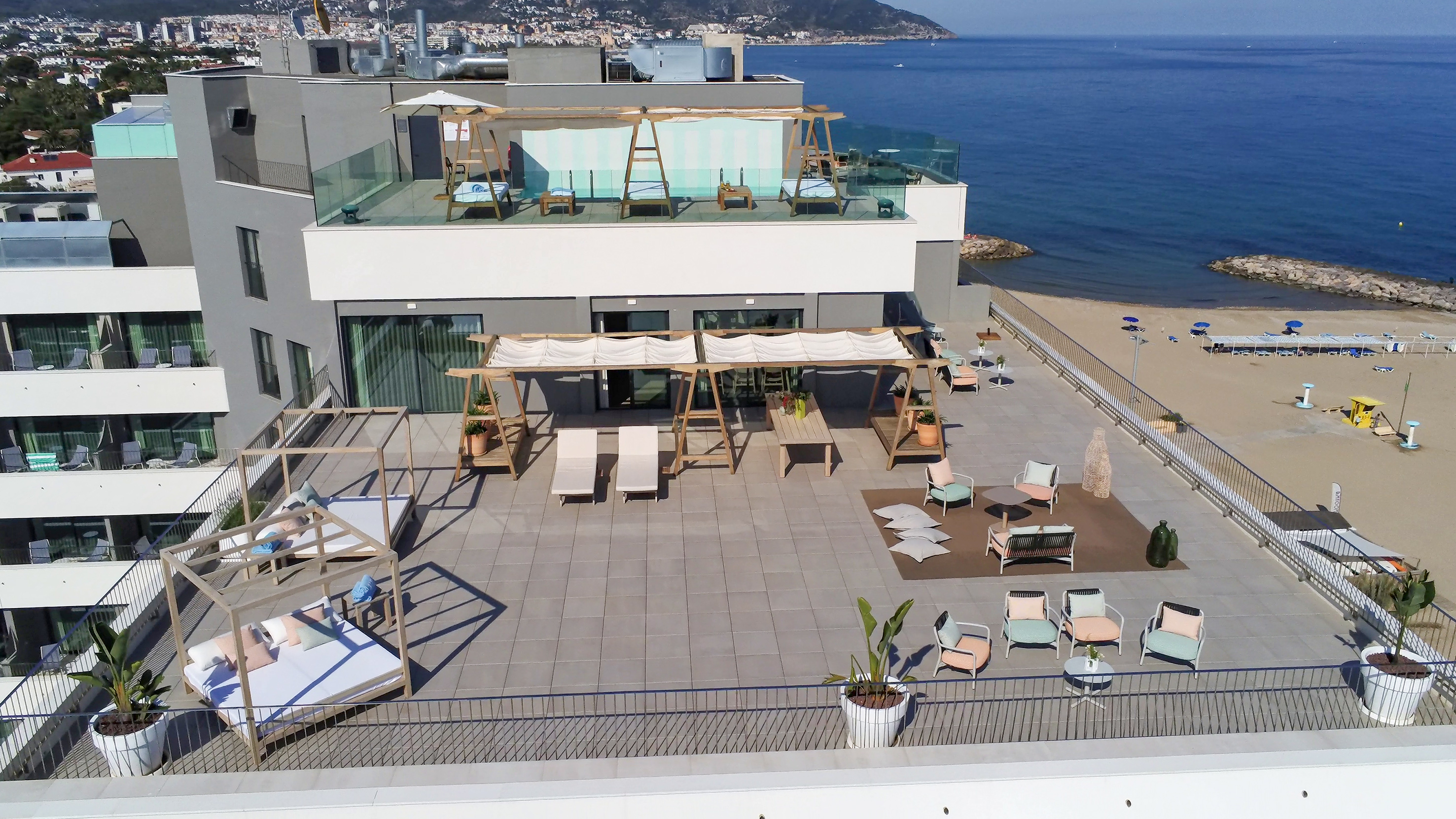 Rooftop terrace overlooking sunny beach and sea, modern hotel outdoor lounge.