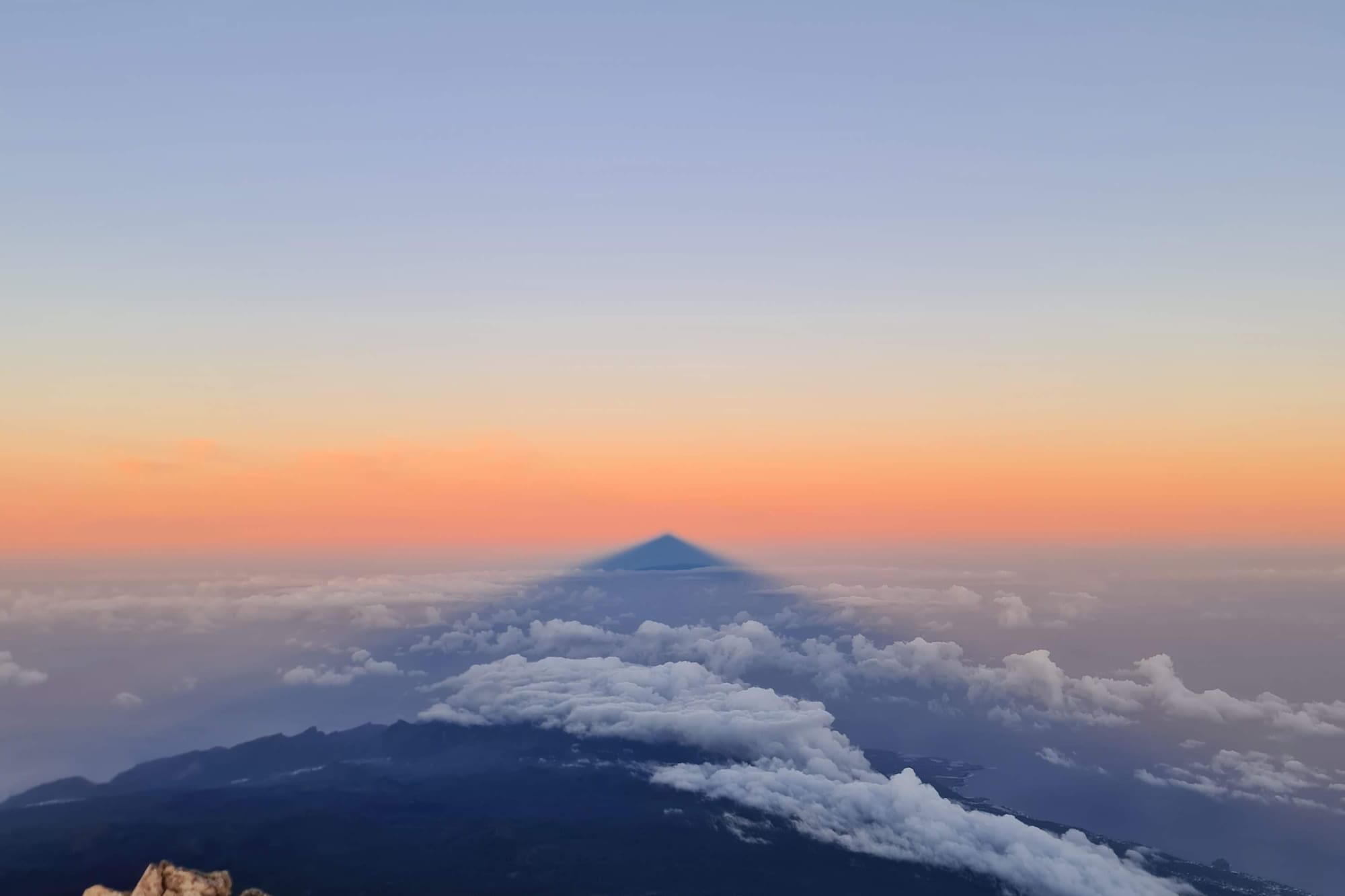 Sombra del Teide al amanecer sobre mar de nubes. Paisaje volcánico.