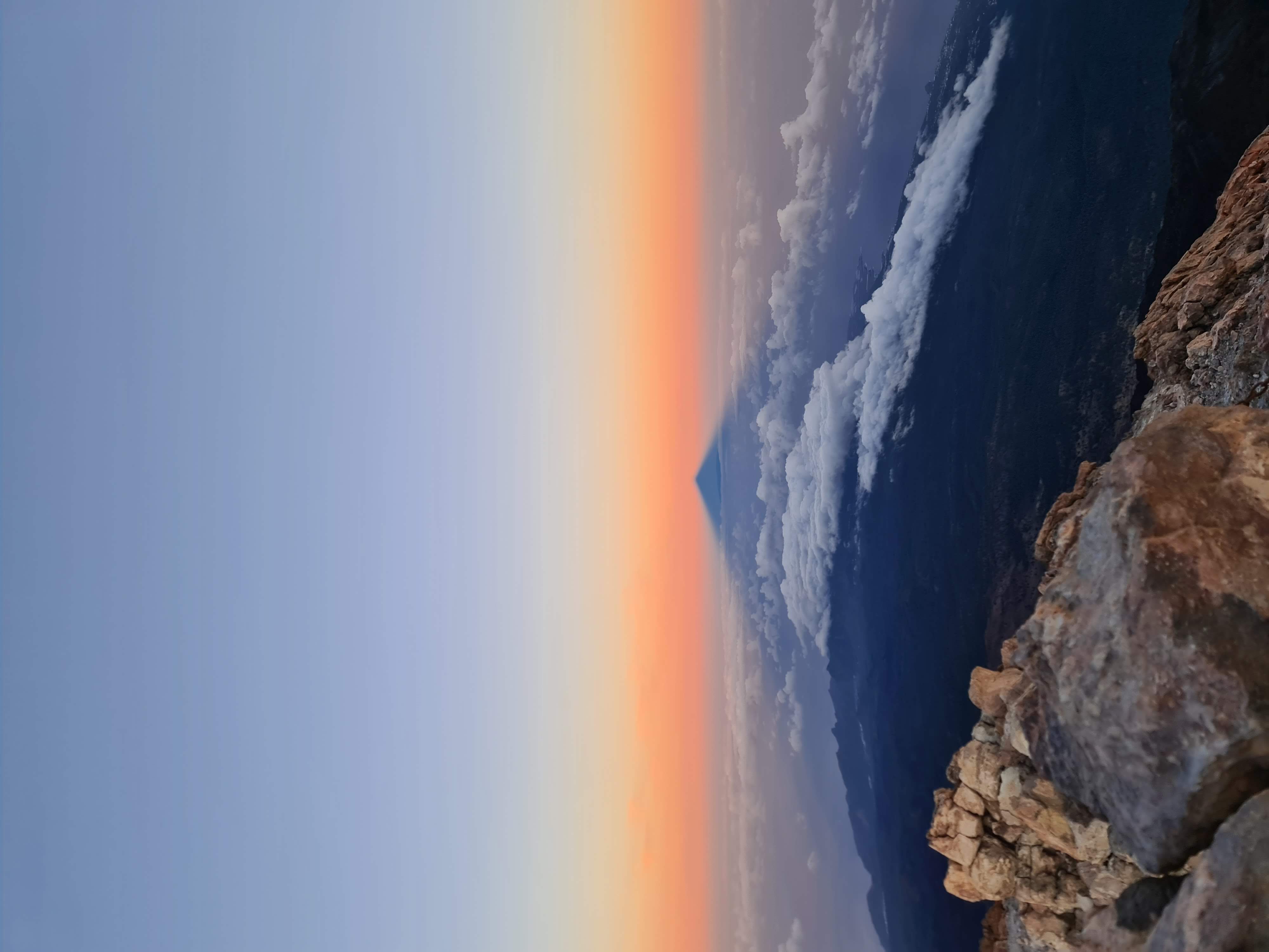 Teide volcano shadow over clouds at sunrise from rocky summit.