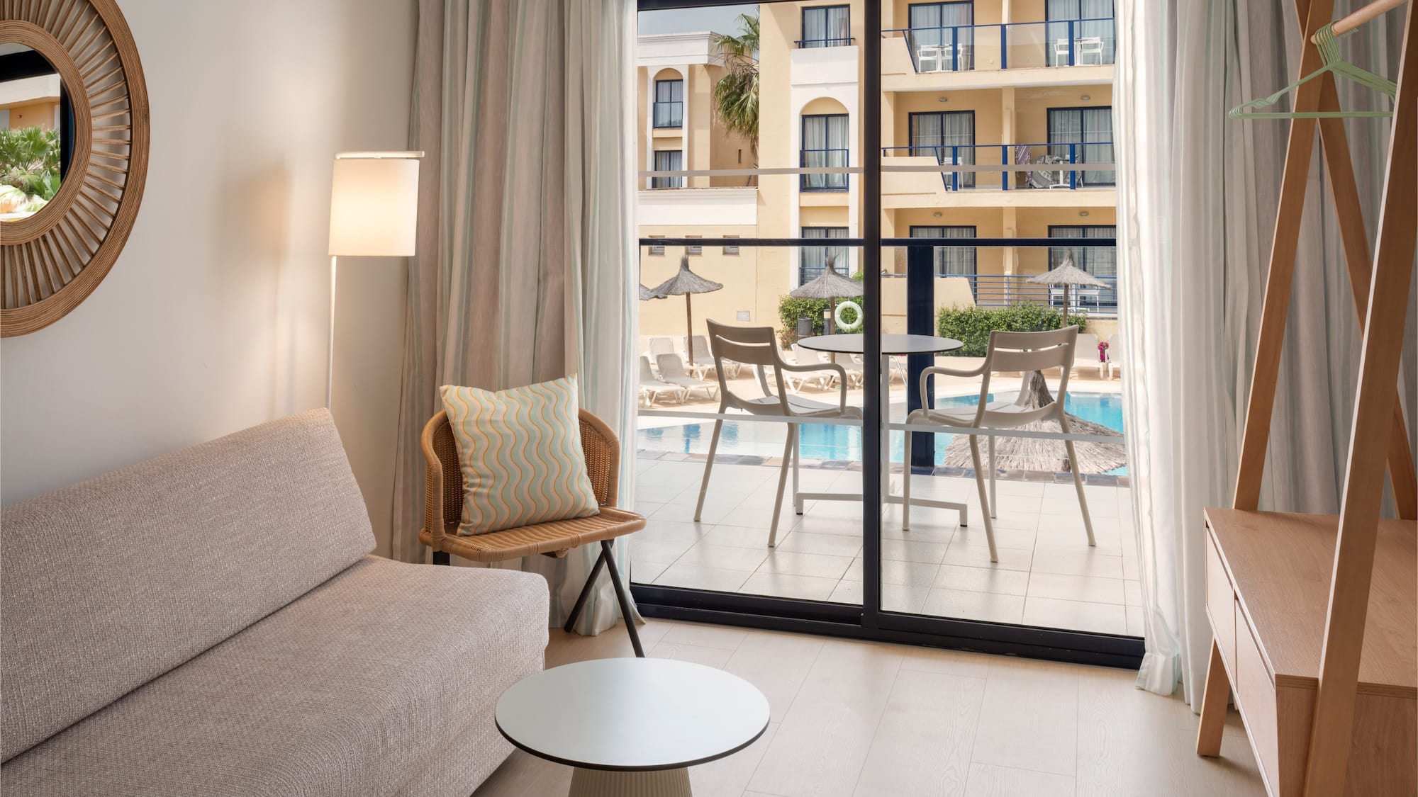 Bright hotel room with pool view balcony, sofa, and modern furniture.