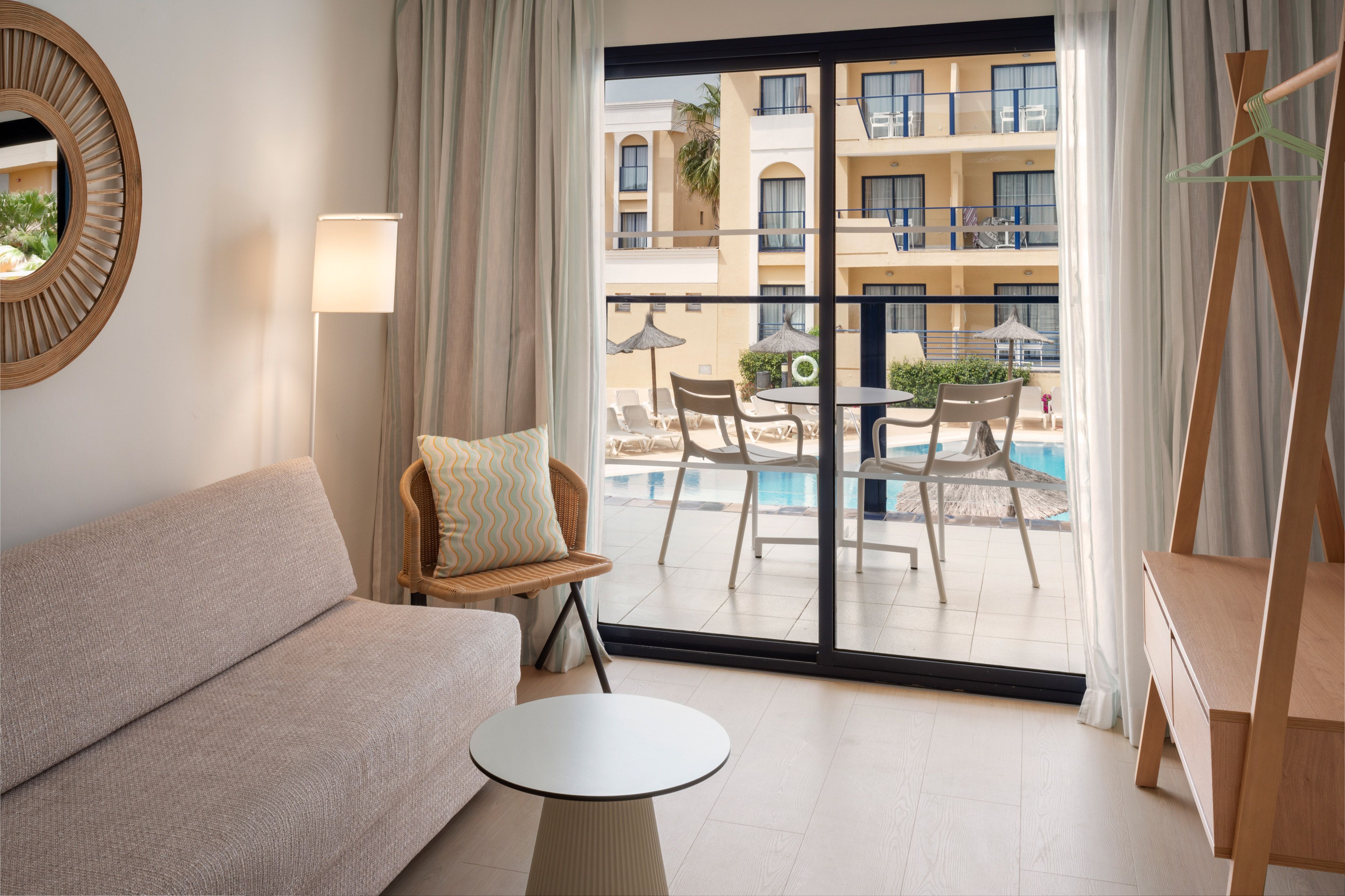 Bright hotel room with pool view balcony, sofa, and modern furniture.