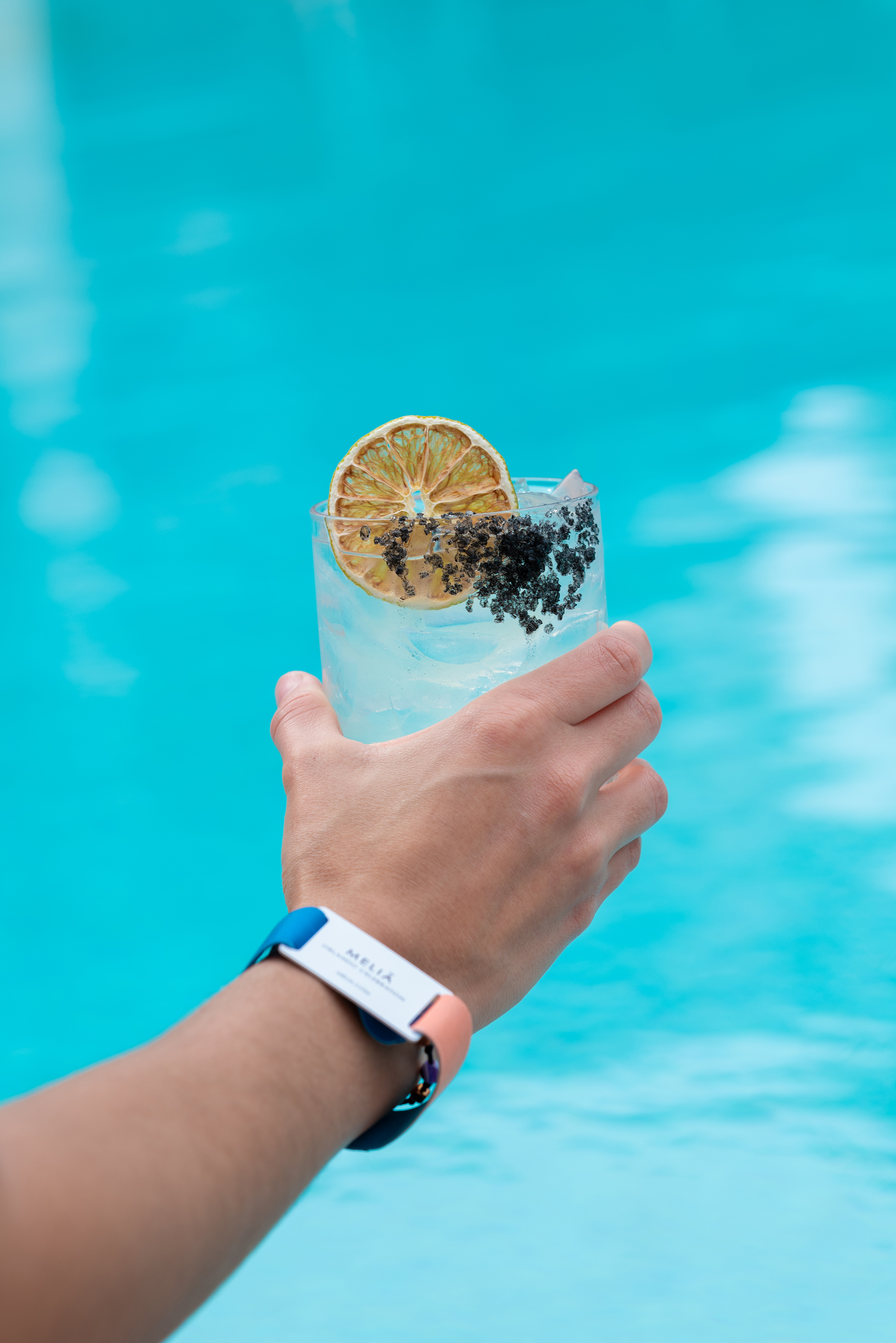 a hand holding a glass of water with a slice of lemon and black poppy seeds