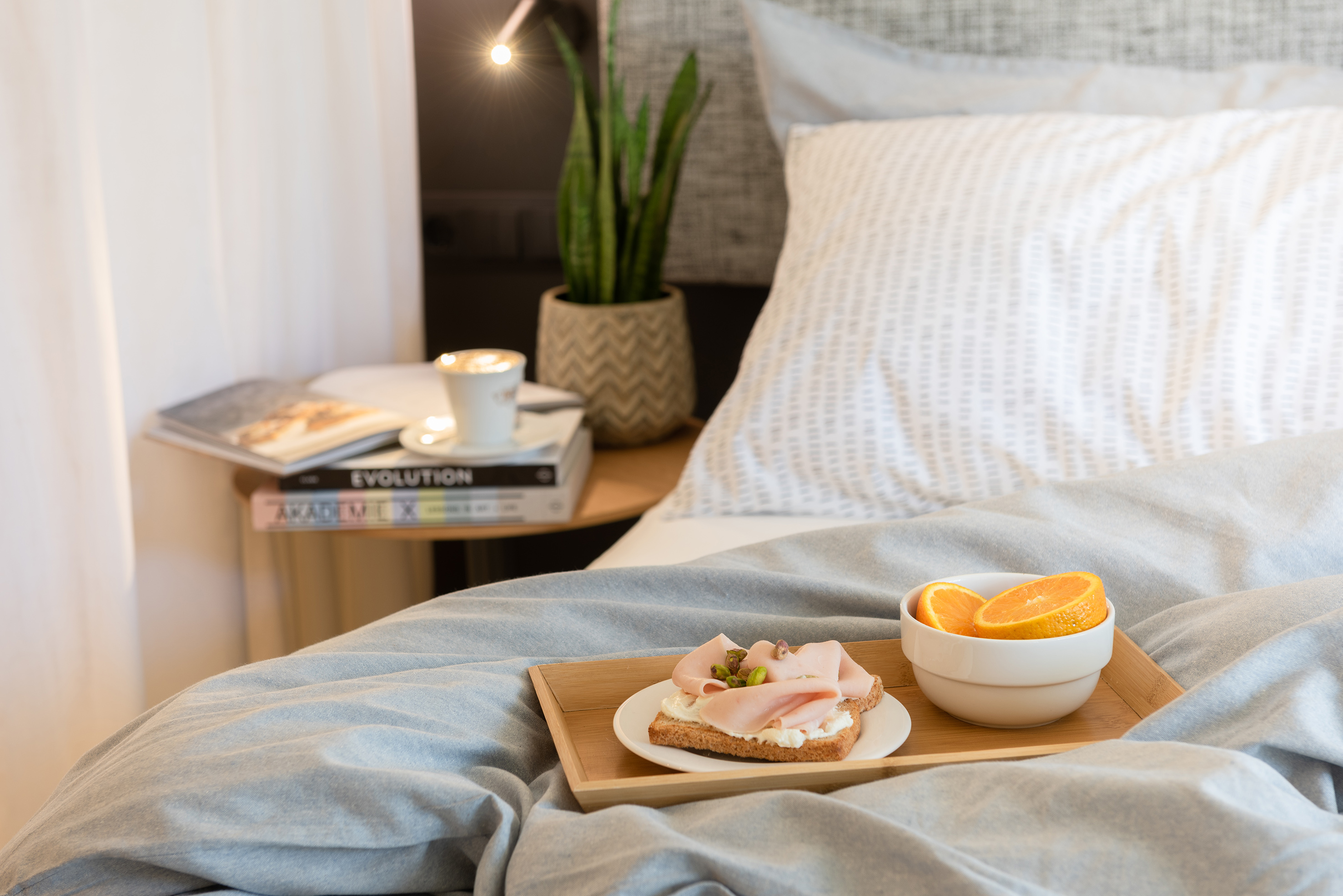 Cozy breakfast in bed with mortadella sandwich, oranges, and coffee.