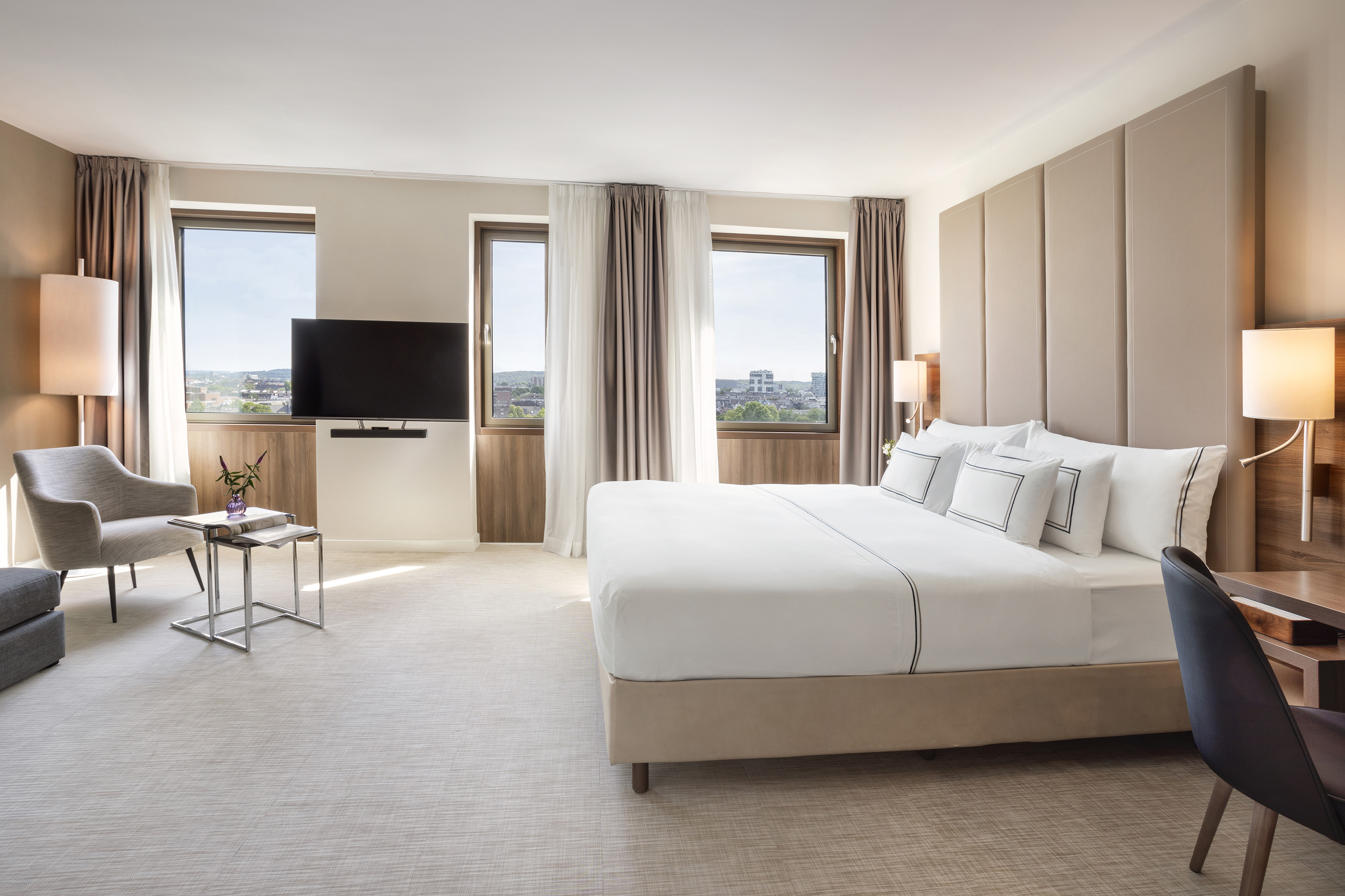 Elegant hotel bedroom featuring a king bed, city view, TV, and sitting area.