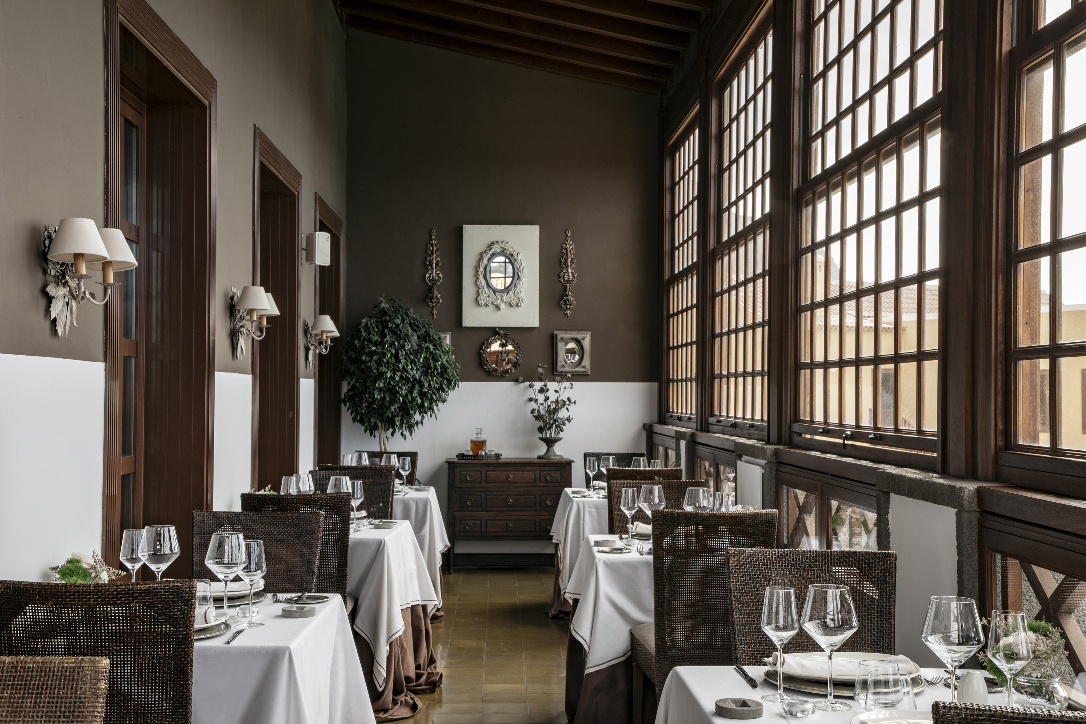Elegant restaurant interior, set tables, wicker chairs, tall paneled windows.