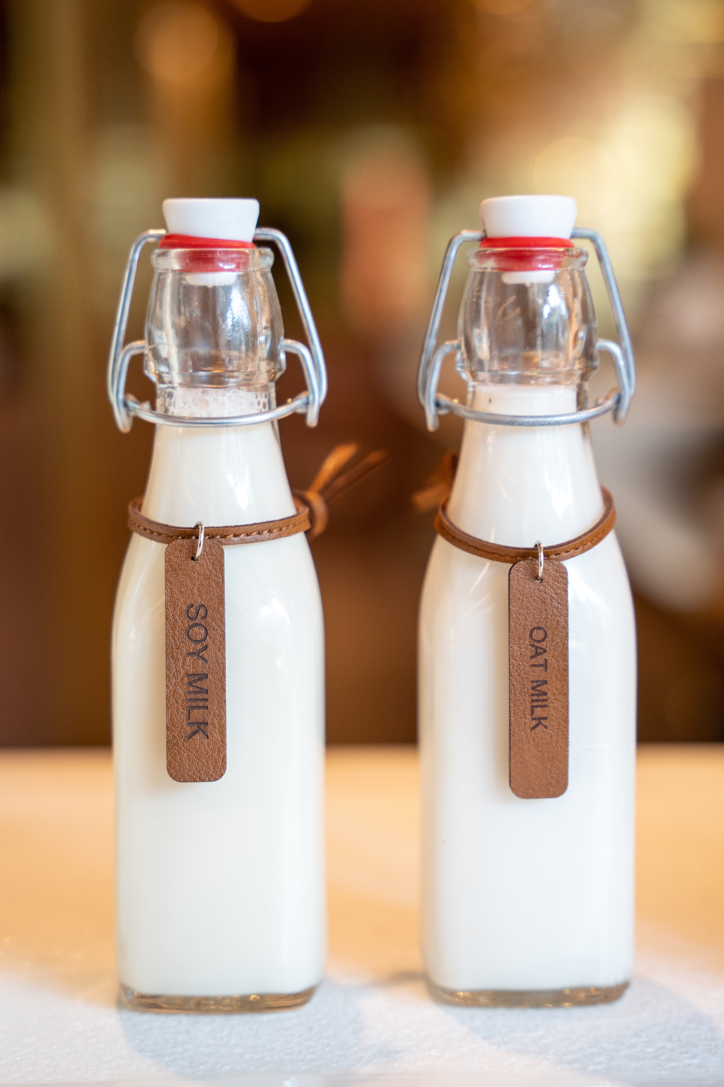 Two swing-top glass bottles containing soy milk and oat milk with leather tags.