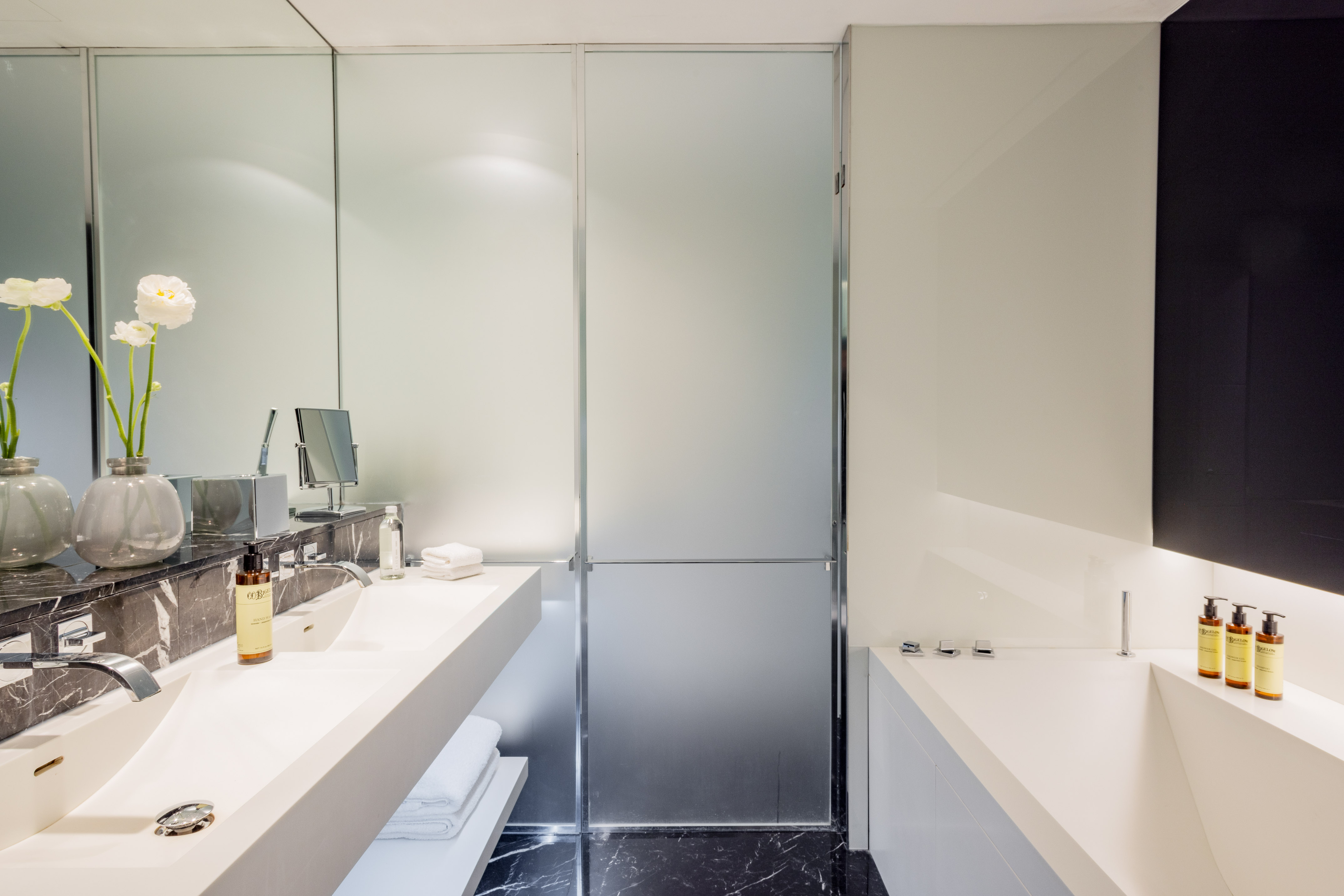 Modern luxury bathroom with double vanity, frosted shower, and white tub.