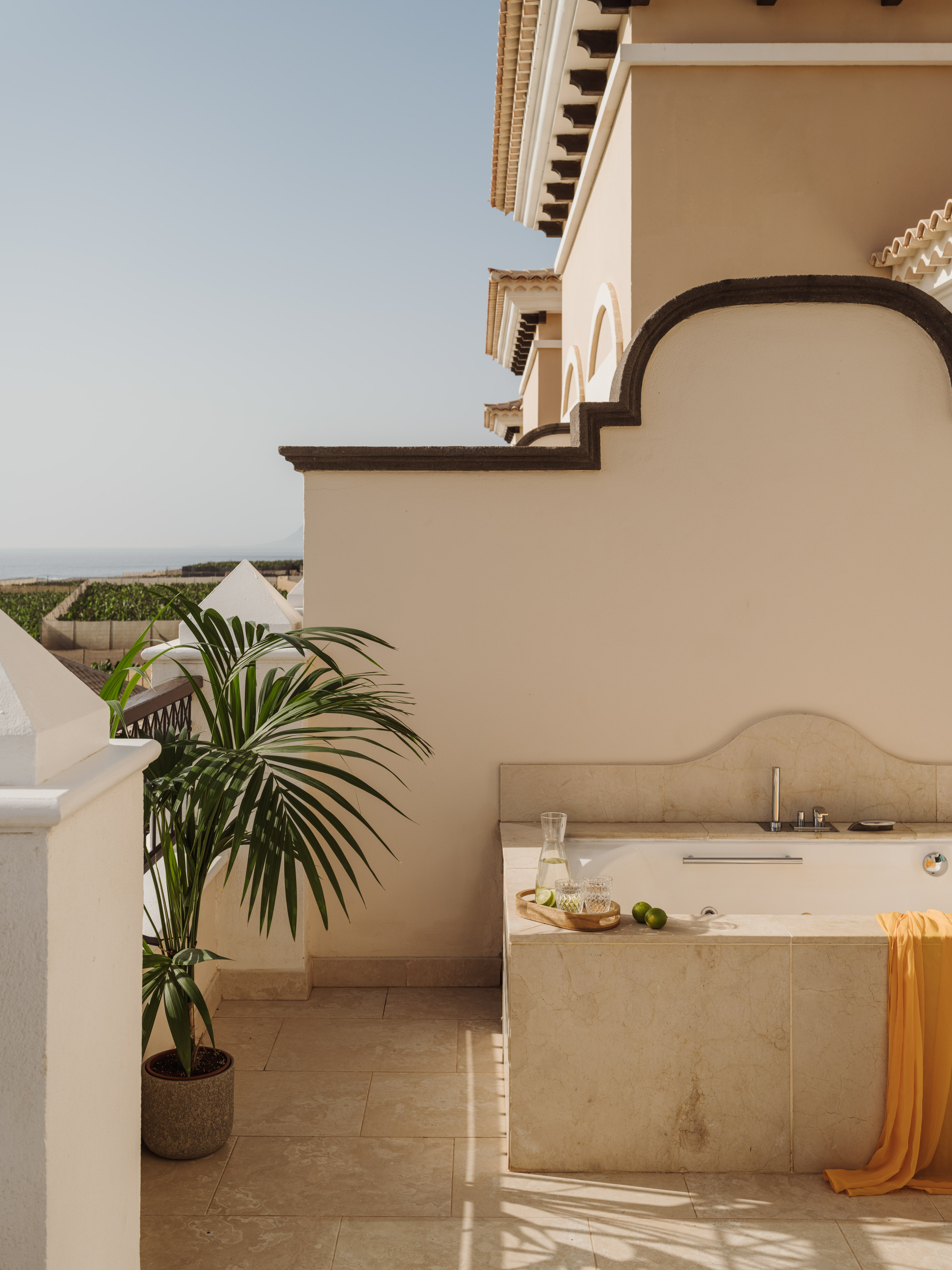 Outdoor bathtub on resort terrace with ocean view, palm, water, and limes.