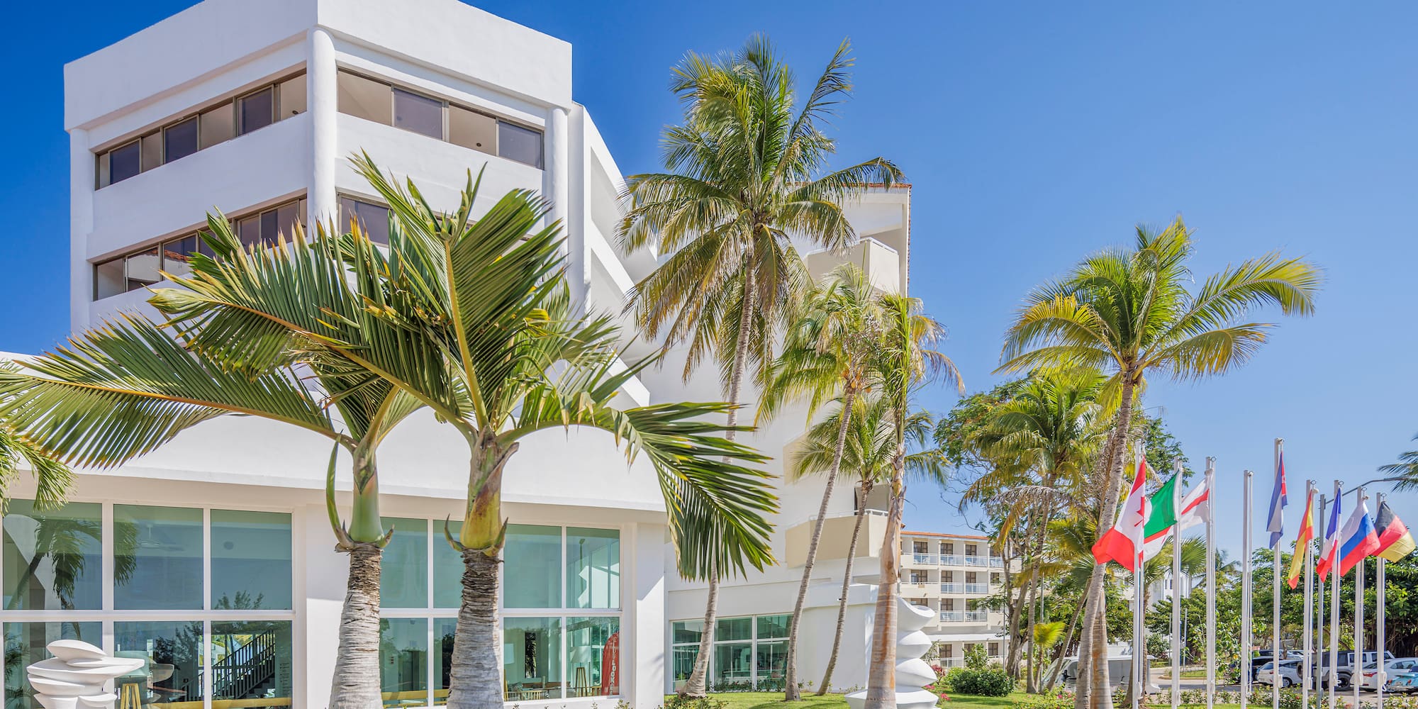 a white building with palm trees and flags