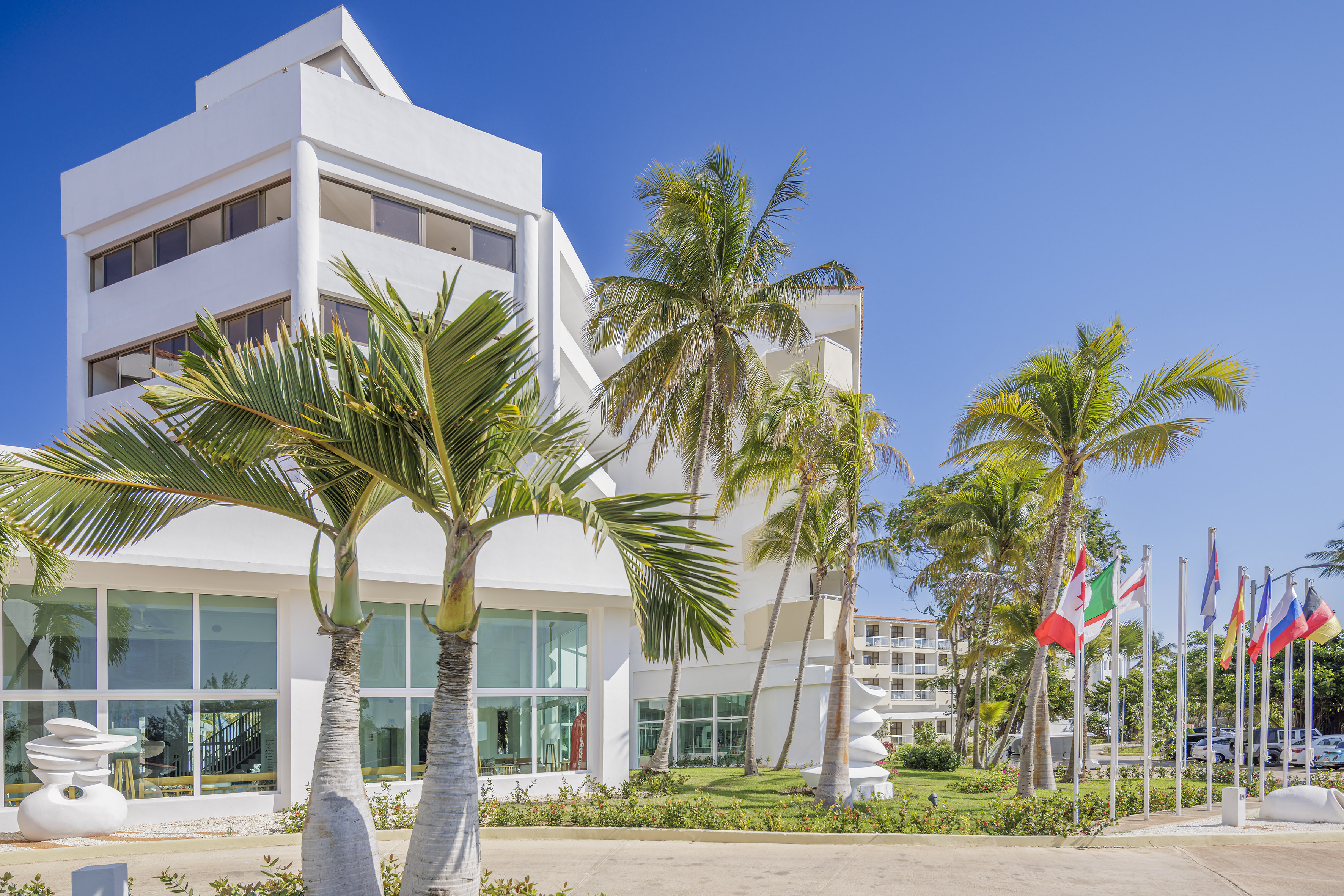a white building with palm trees and flags