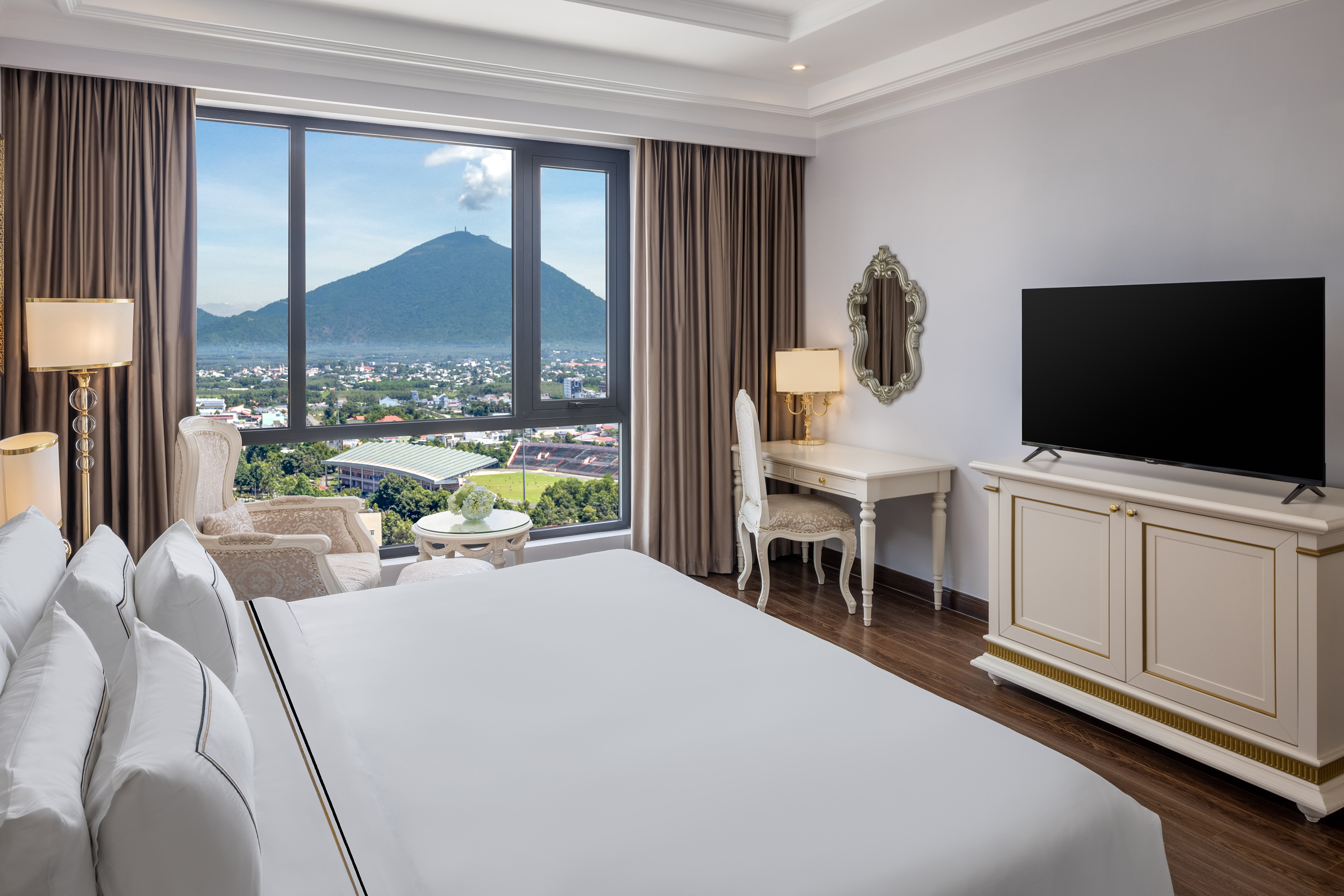Luxury hotel room with mountain and city view, king bed, and desk.