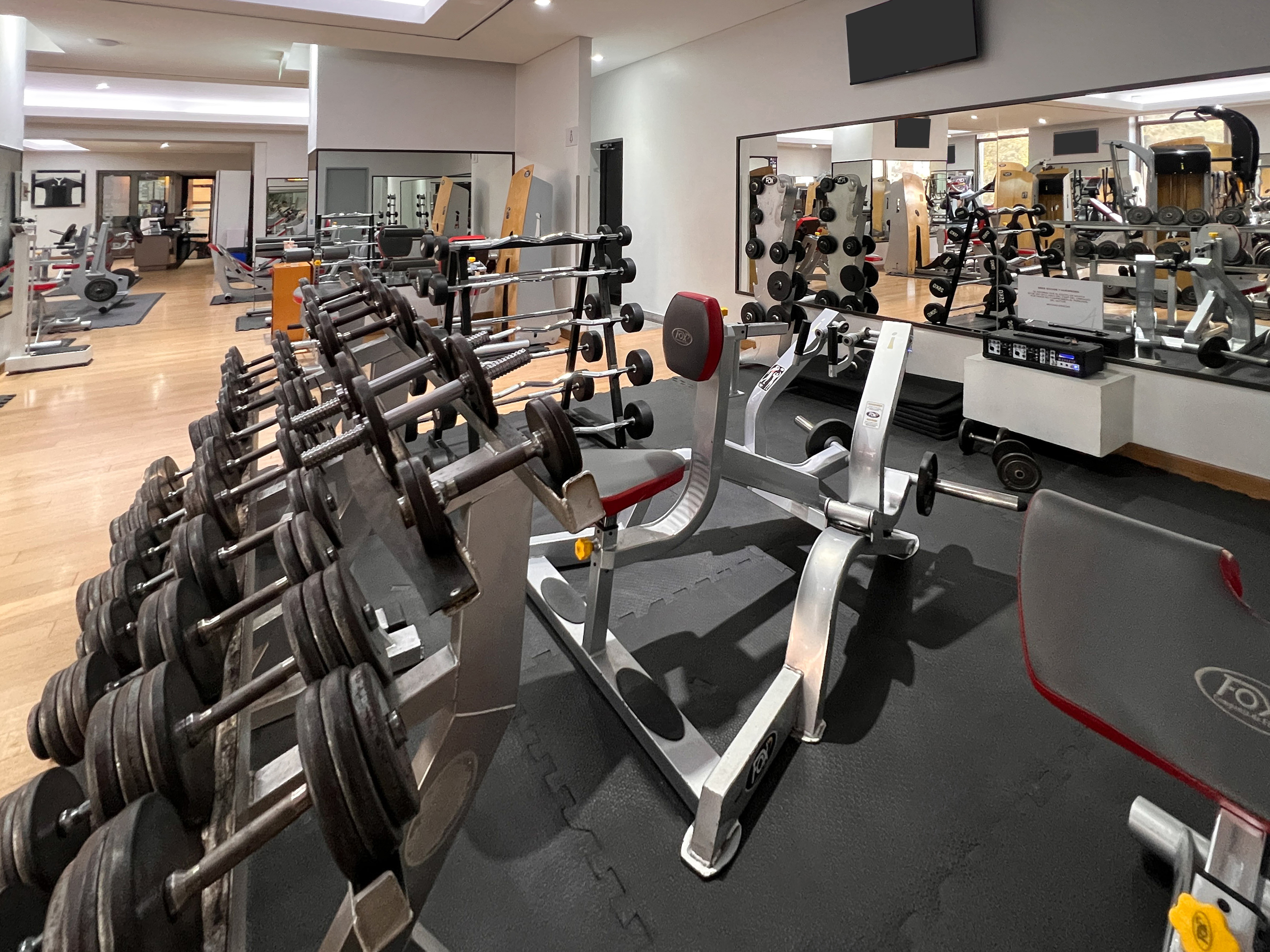 Gym floor with dumbbell racks, weight benches, and fitness equipment.