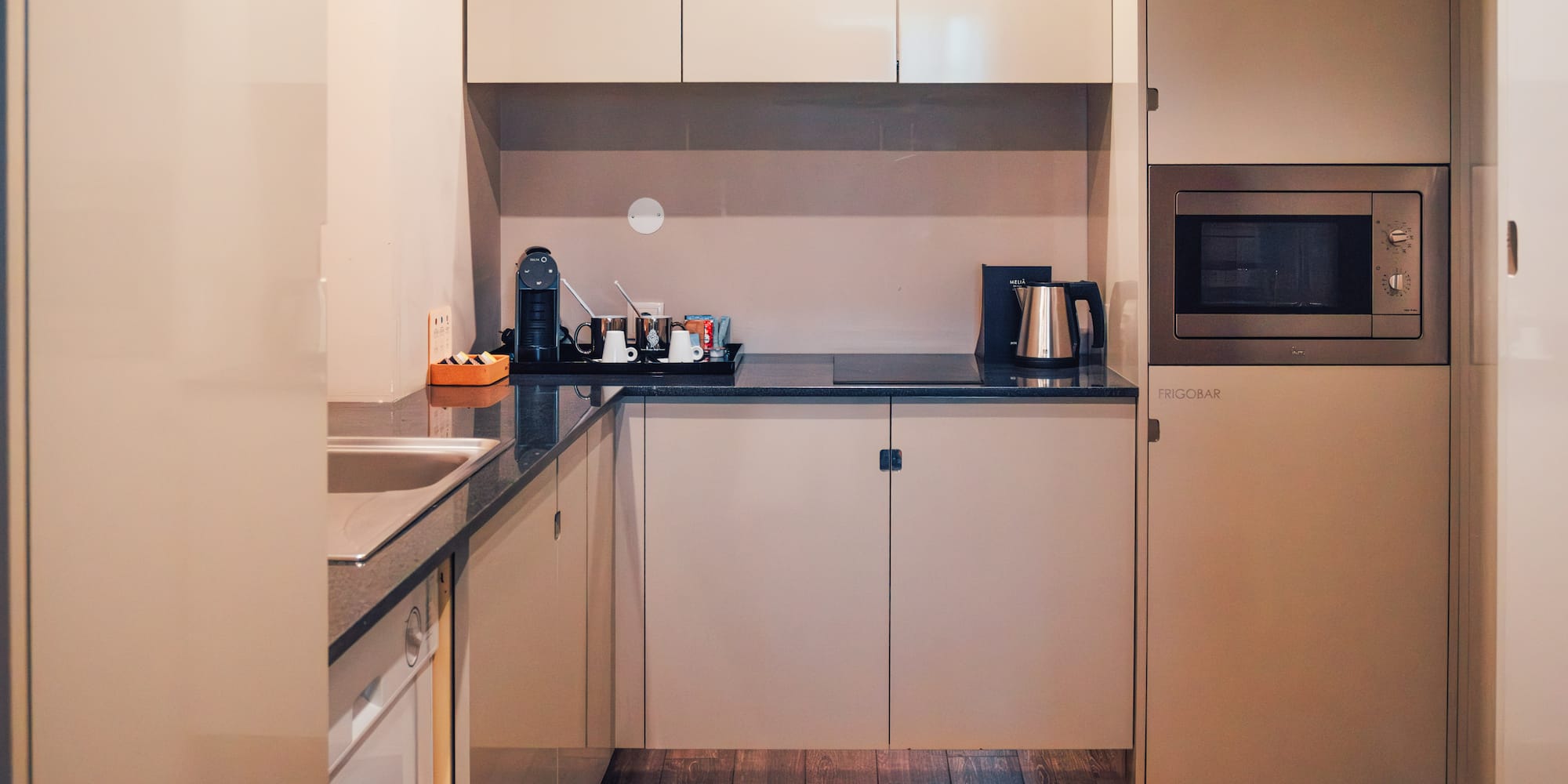 Modern compact kitchen with beige cabinets, microwave, coffee maker, frigobar.