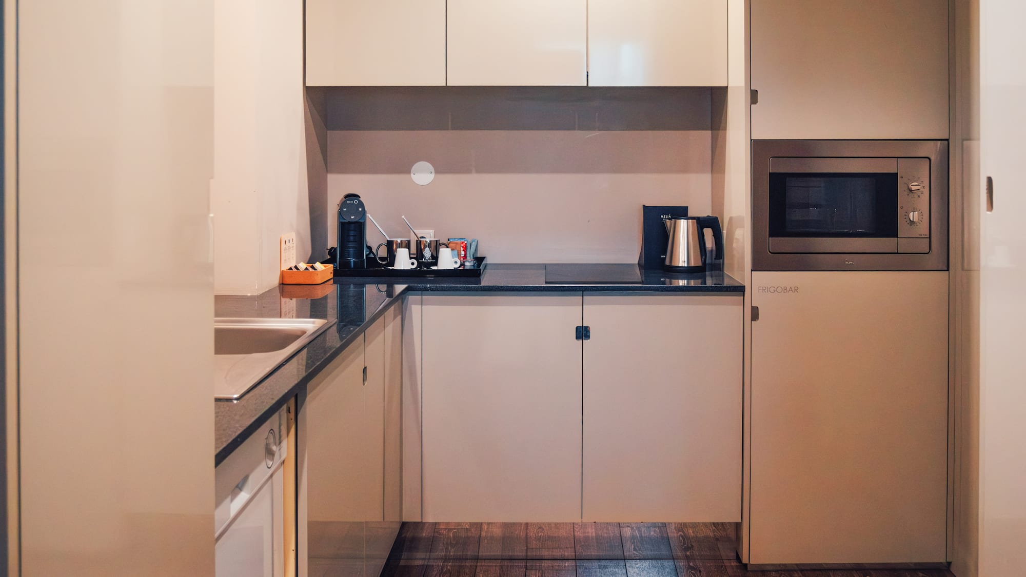 Modern compact kitchen with beige cabinets, microwave, coffee maker, frigobar.