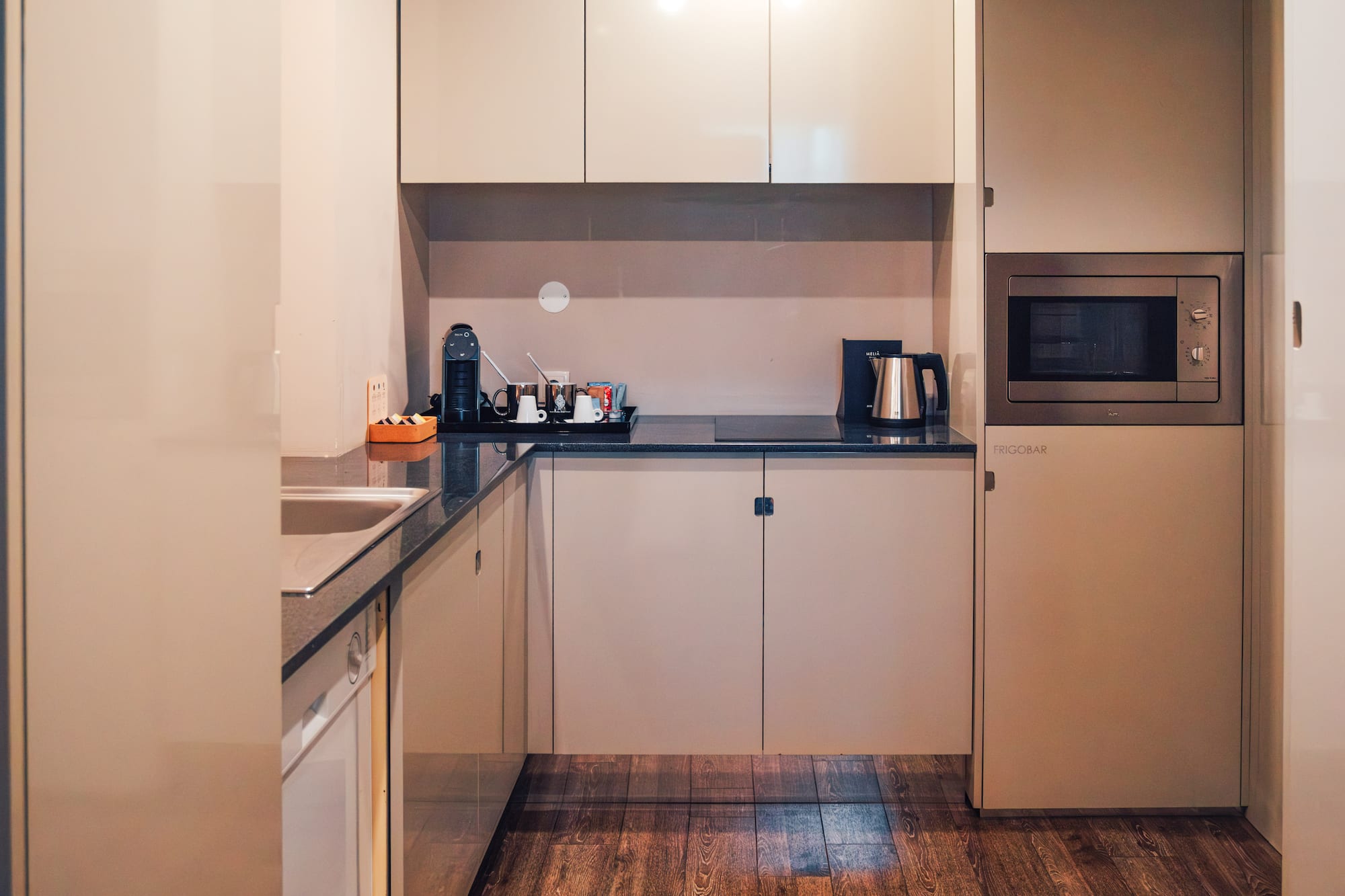 Modern compact kitchen with beige cabinets, microwave, coffee maker, frigobar.