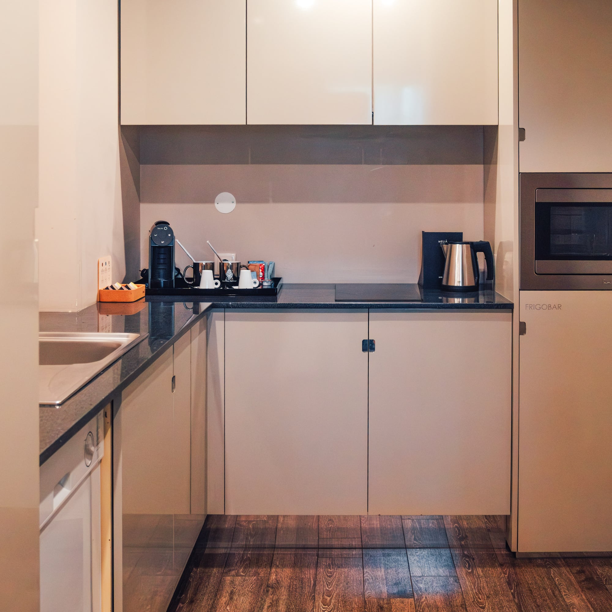 Modern compact kitchen with beige cabinets, microwave, coffee maker, frigobar.