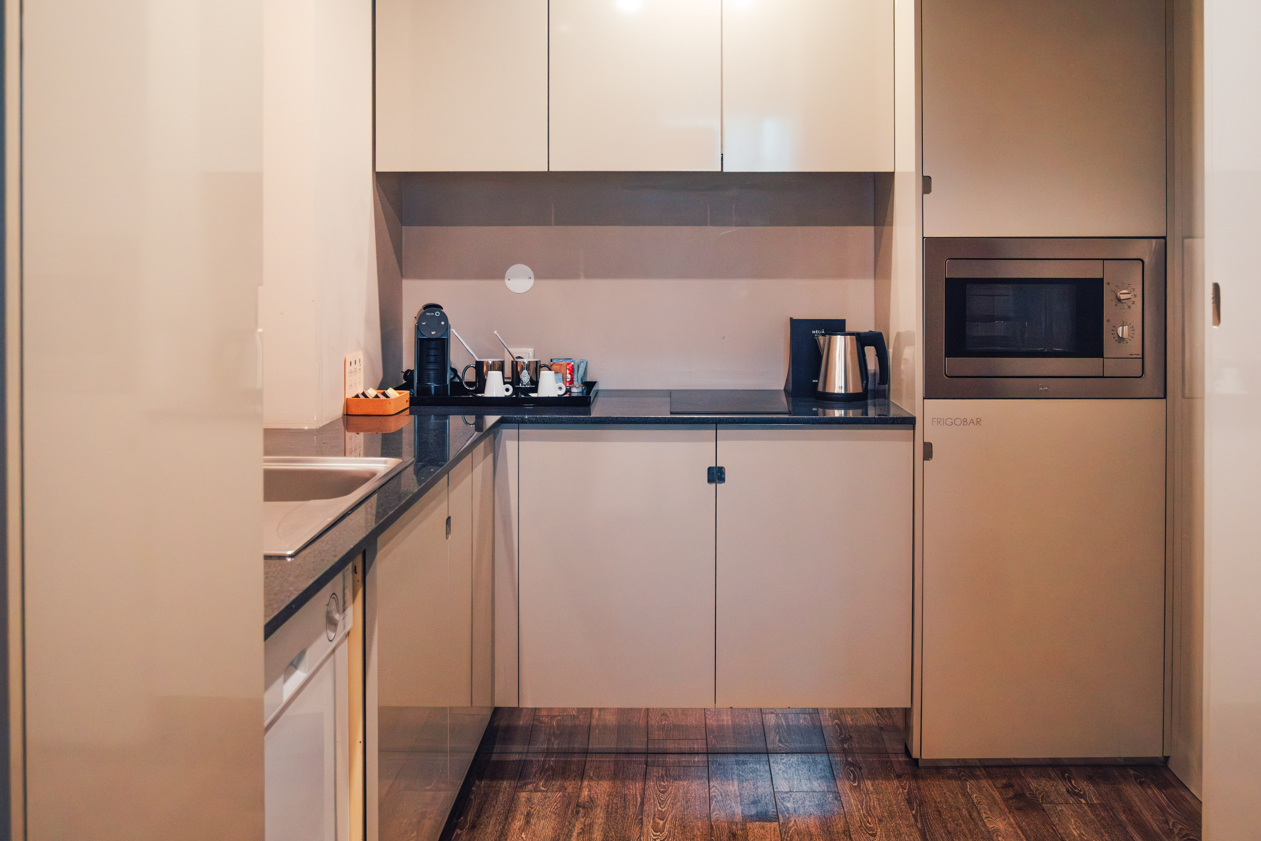 Modern compact kitchen with beige cabinets, microwave, coffee maker, frigobar.
