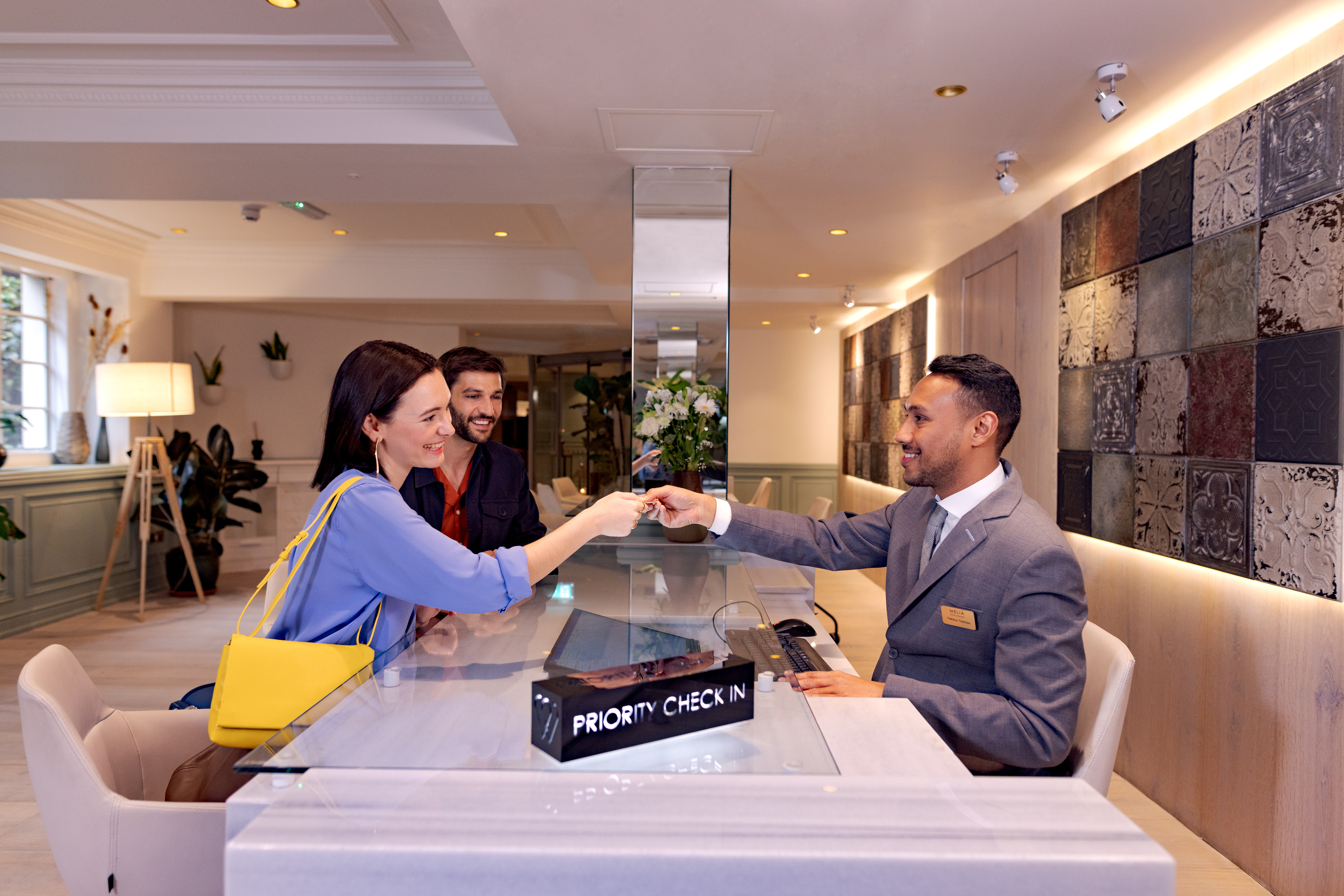 Hotel receptionist hands key card to smiling guests at priority check-in desk.