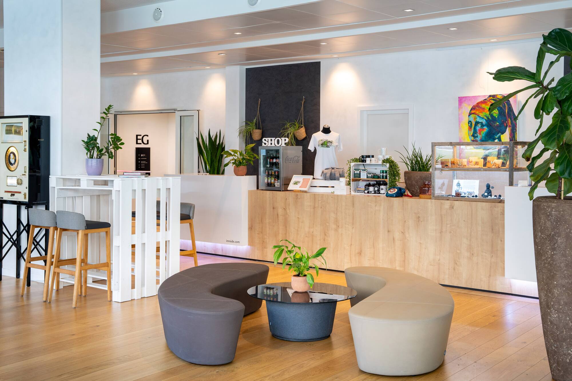 Modern lobby shop, wooden counter, plants, and stylish lounge seating.