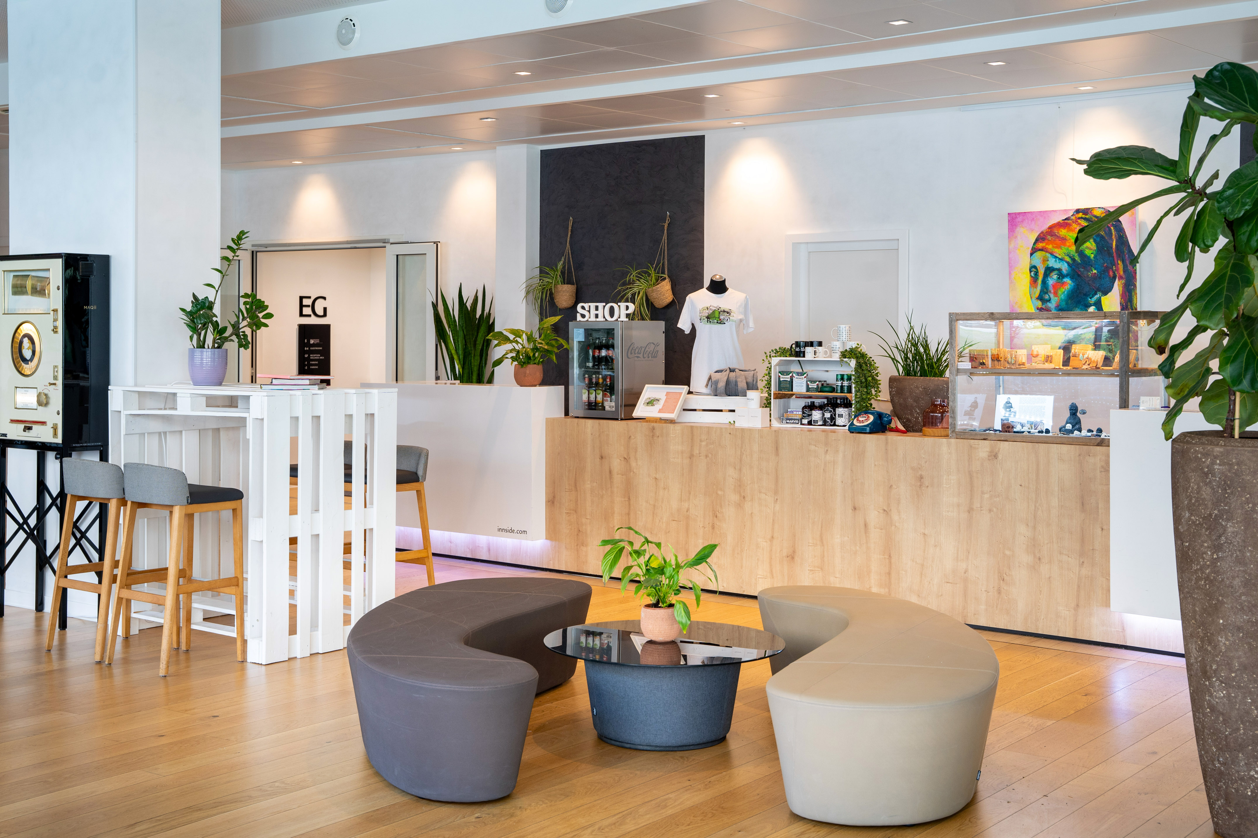 Modern lobby shop, wooden counter, plants, and stylish lounge seating.