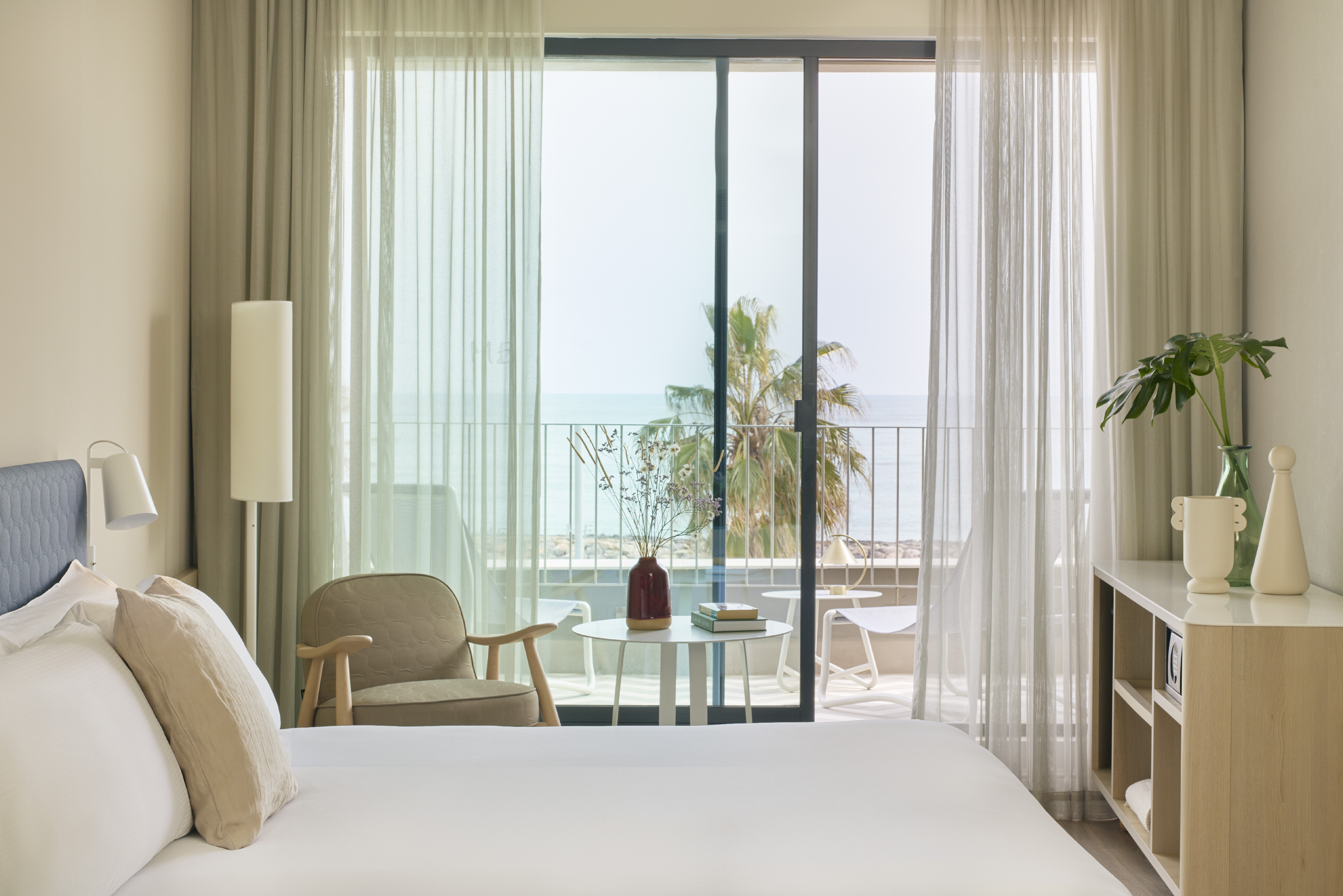 Modern hotel bedroom with ocean view balcony, white bed, and minimalist decor.