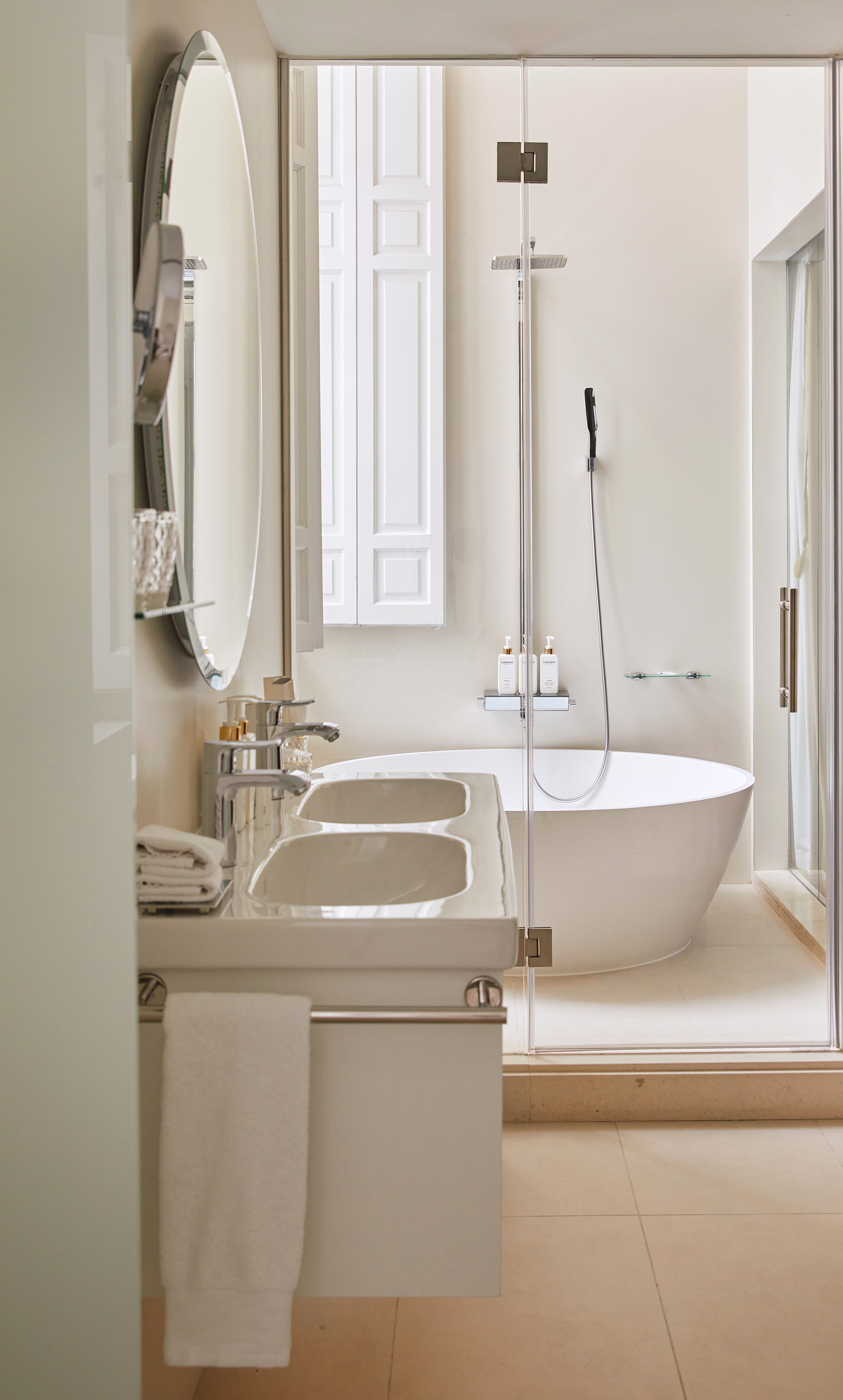 Modern bathroom: dual sinks, oval mirror, freestanding tub, glass shower.
