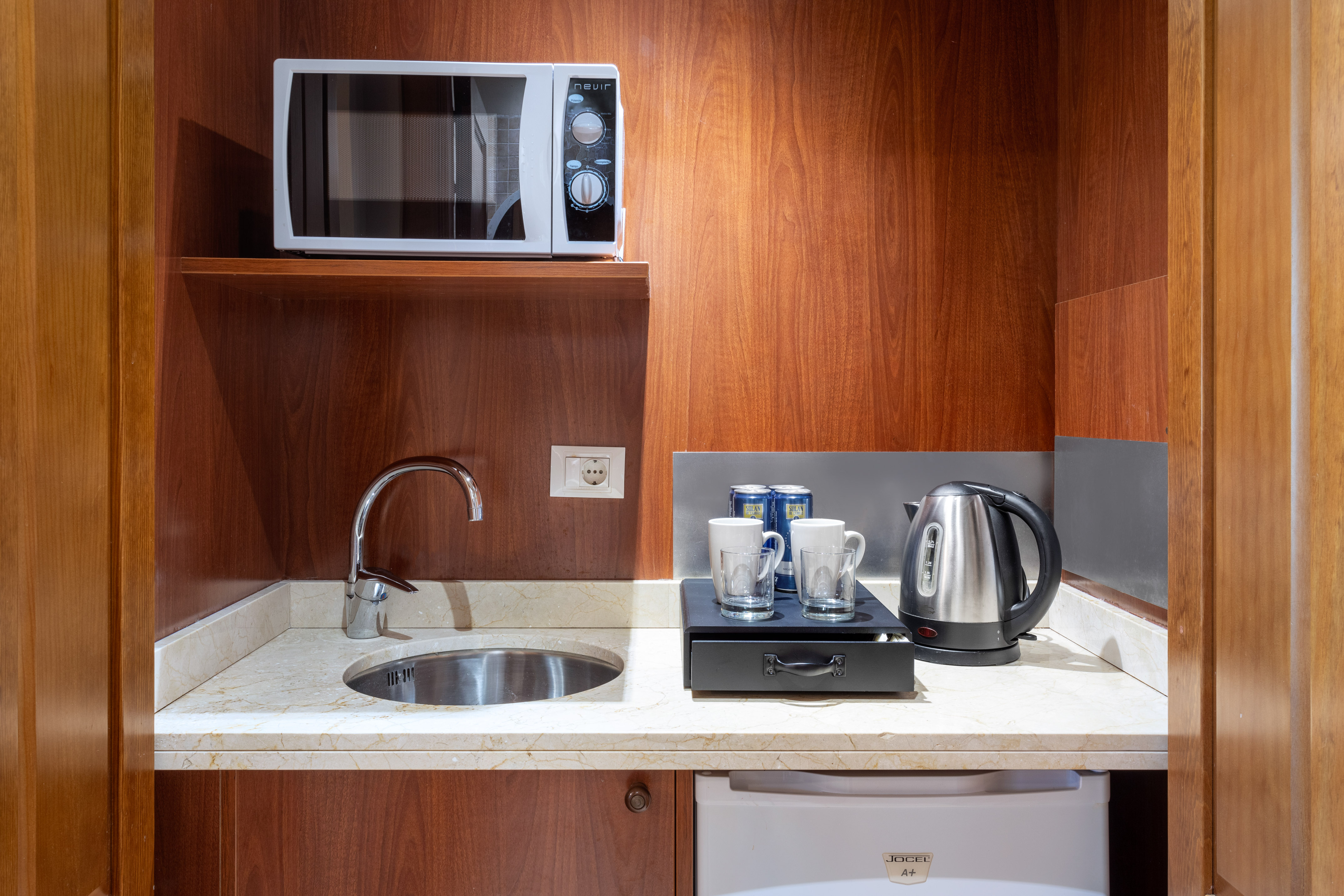 Compact hotel kitchenette featuring microwave, sink, kettle, and mini-fridge.