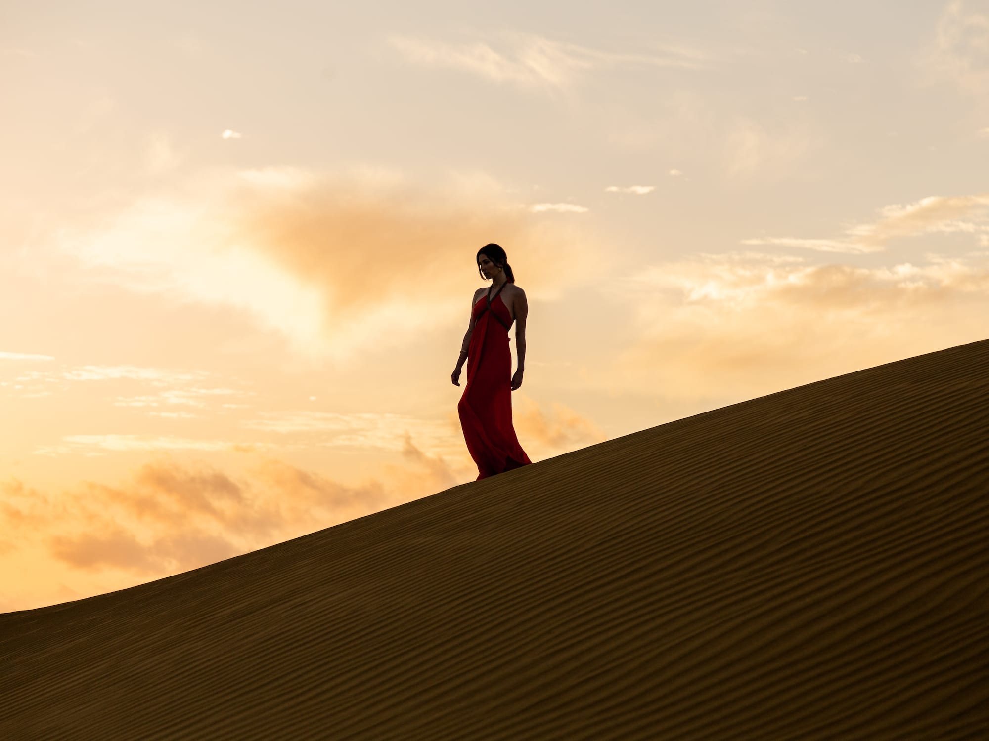 a woman in a red dress walking up a sand dune